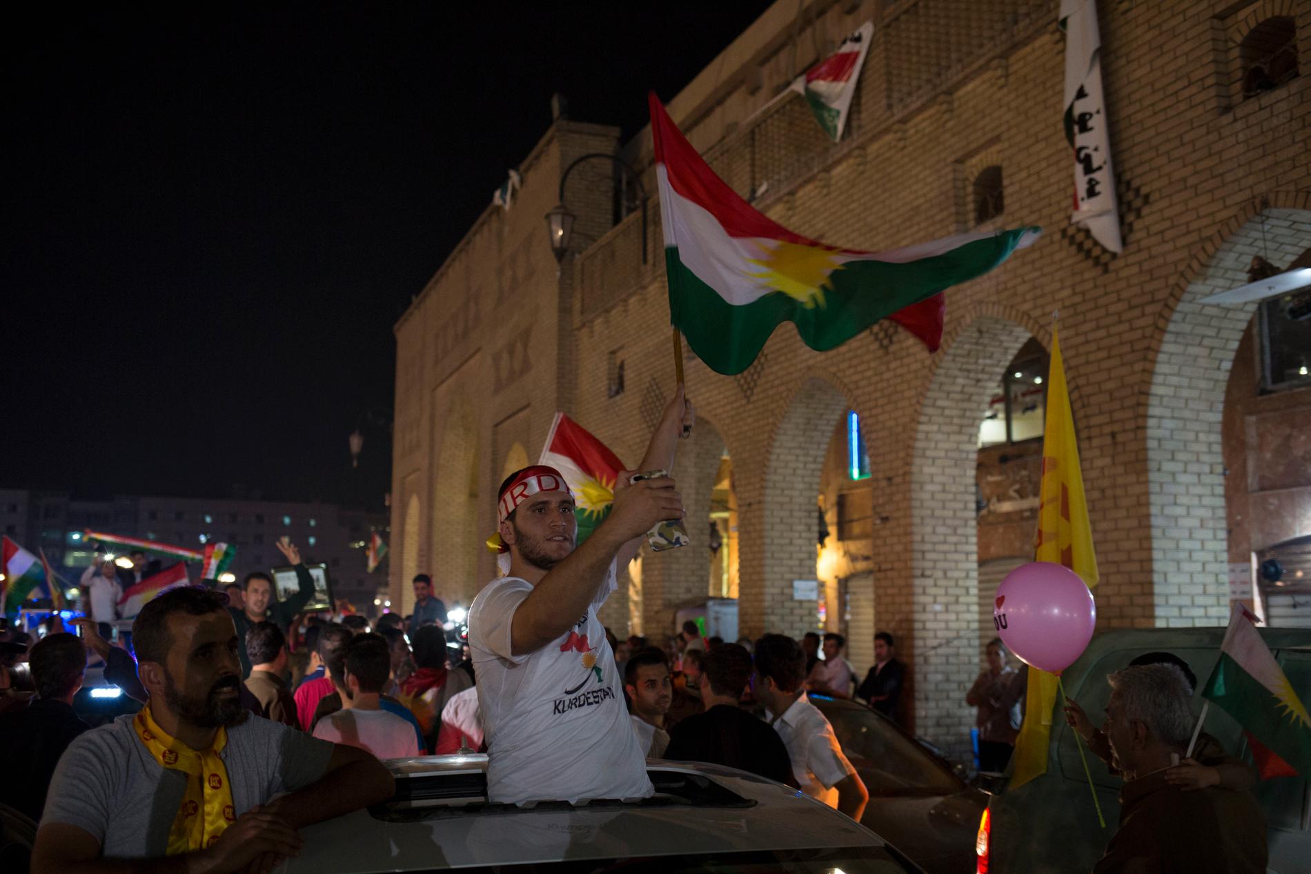 En man viftar med en kurdisk flagga utanför en vallokal.
