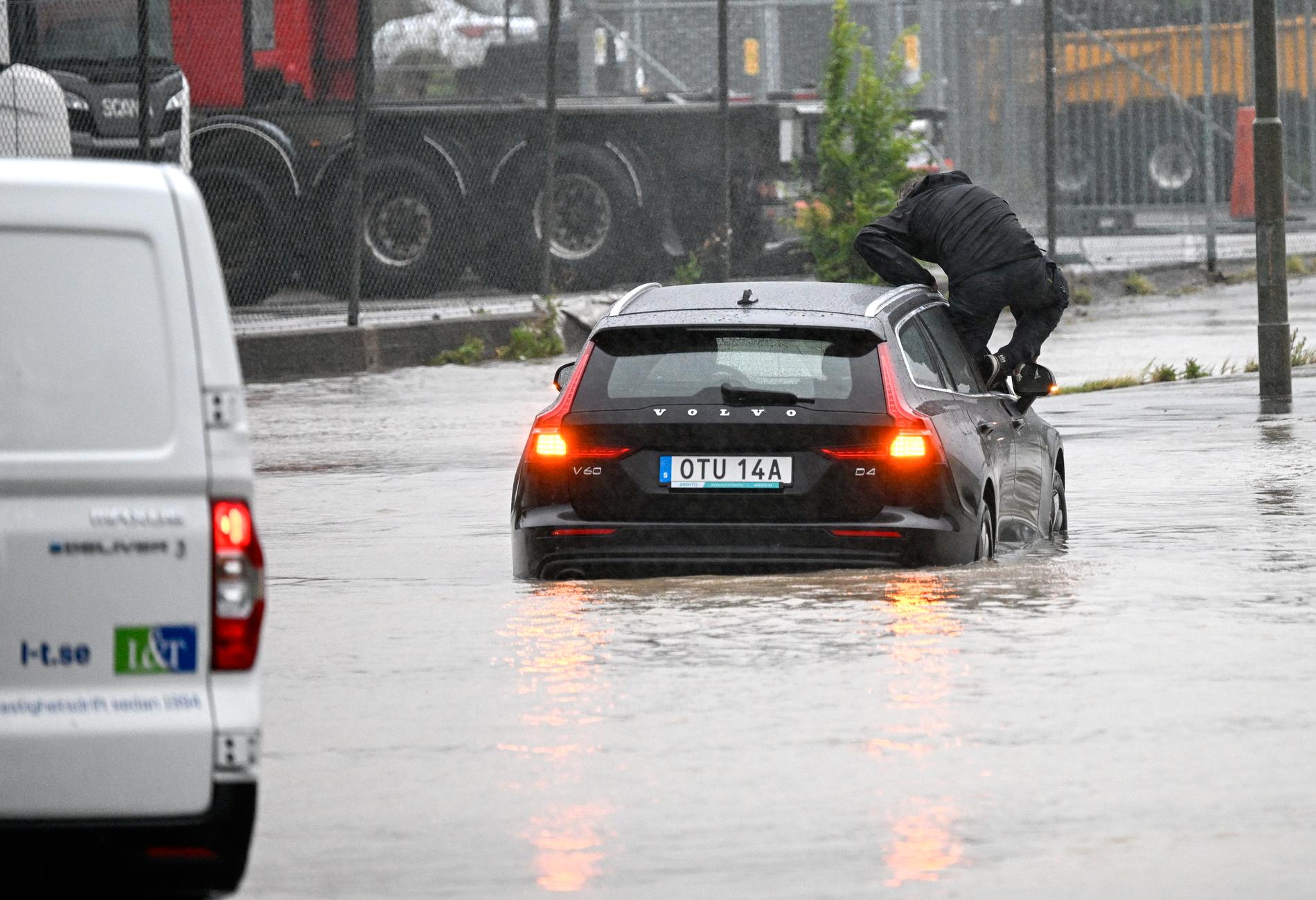 En man klättrar ut en bil som försökte ta sig genom en översvämmad rondell i Arlöv vid den avstängda översvämmade Västkustvägen E6 utanför Malmö under ovädret Hans. Arkivbild.