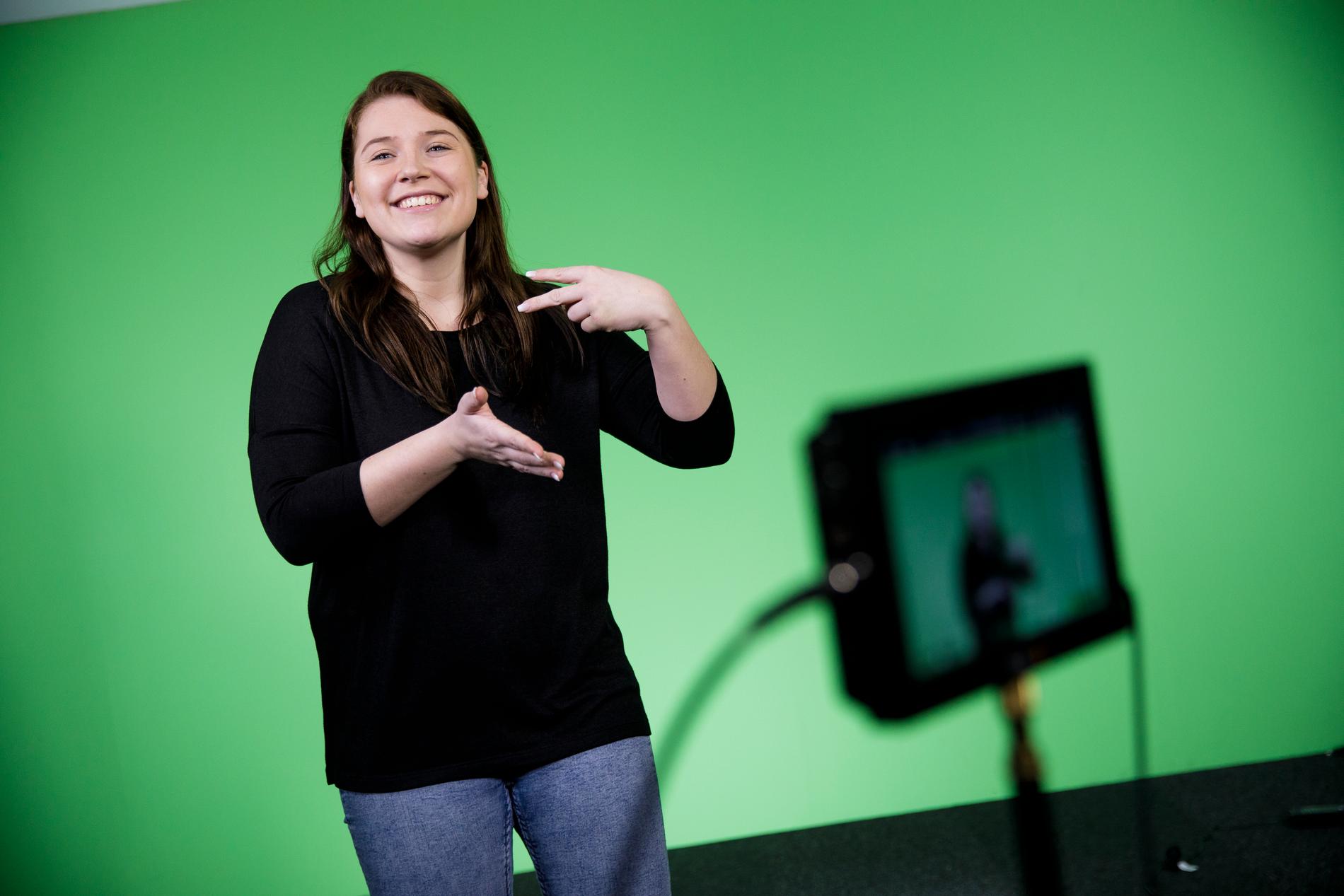 Jade Osbeck teckenspråksgestaltar några av låtarna i finalen av Melodifestivalen. Framför en ”green screen” gör hon sin version av låten. 