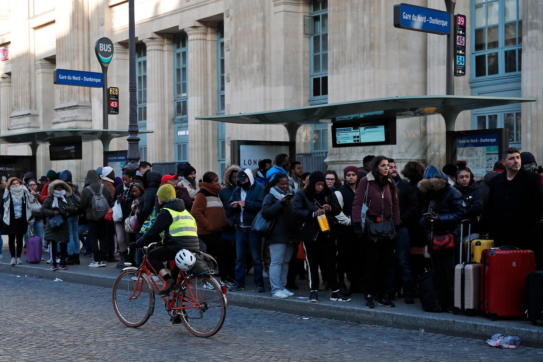 En kvinna cyklar förbi en kö till en buss vid Gare du Nord i Paris. Arkivbild.