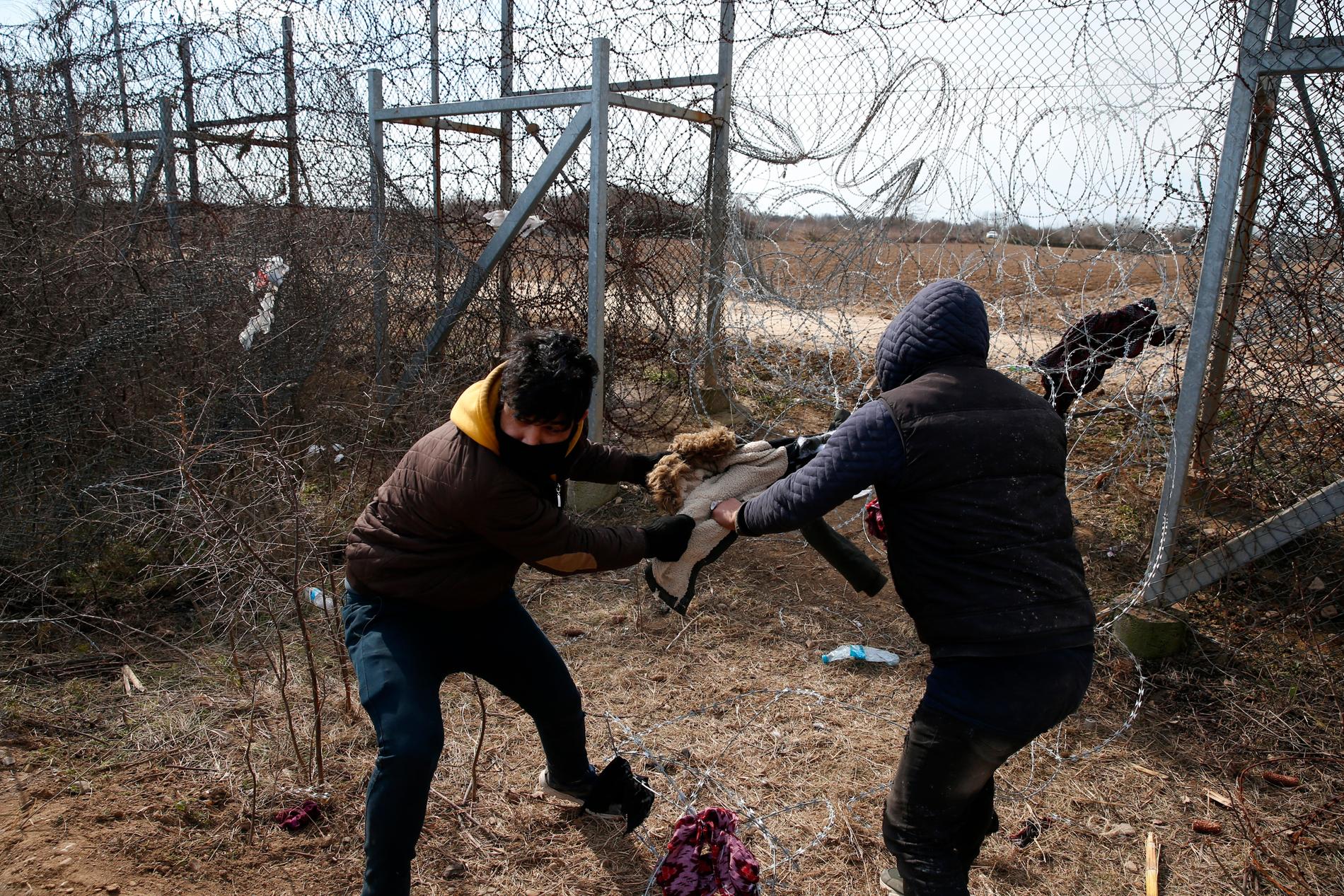Två unga män försöker ta sig igenom taggtråden vid gränsen mellan Turkiet och Grekland.