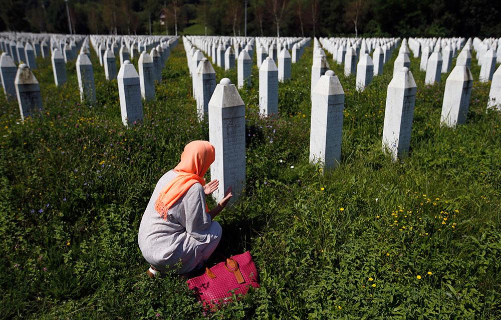 En bosniakisk kvinna knäböjer vid gravplatsen på minnescentret Potocari i Srebrenica.