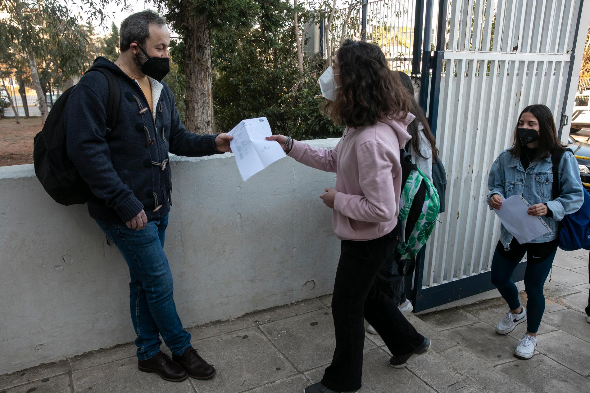 Gymnasieelever visar upp sitt testresultat på väg in i skolan i Atens förorter på måndagen.