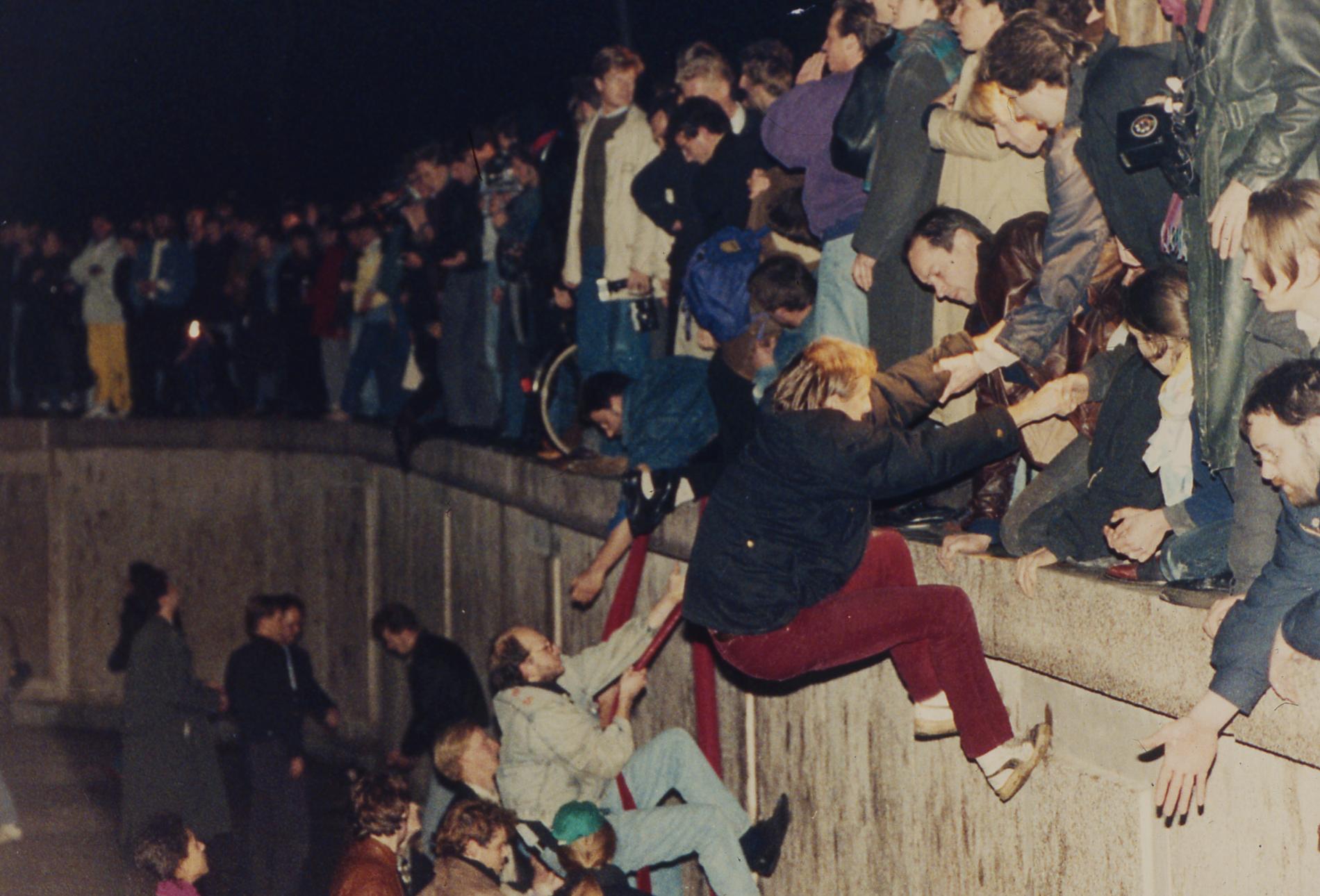 Östberlinare får hjälp av Västberlinare att klättra över muren den 10 november 1989.