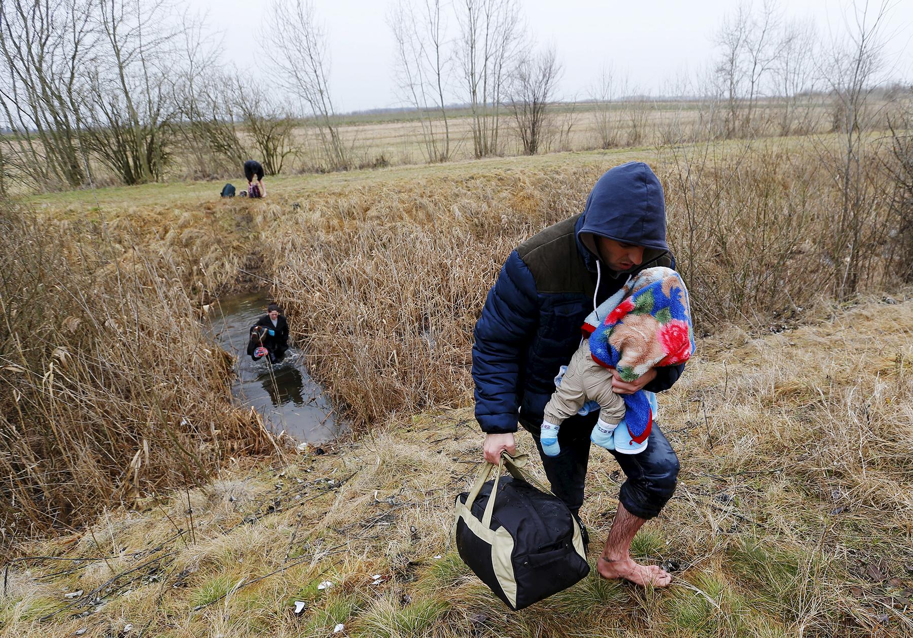 En man bär på sitt barn när han illegalt tar sig in i Ungern från Serbien i februari i år.