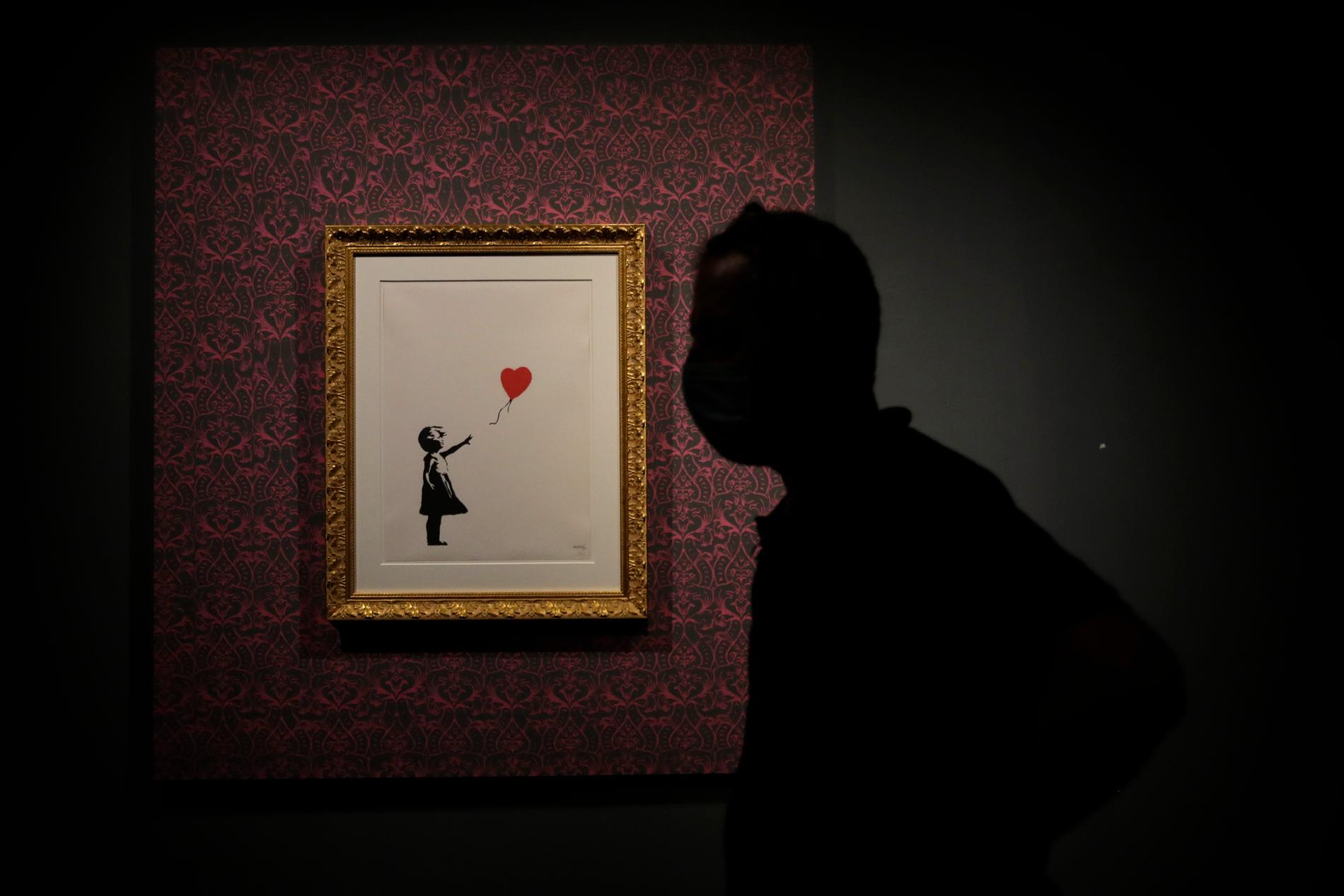 Manlig siluett framför en print av Banksys kända verk ”Girl with balloon”.