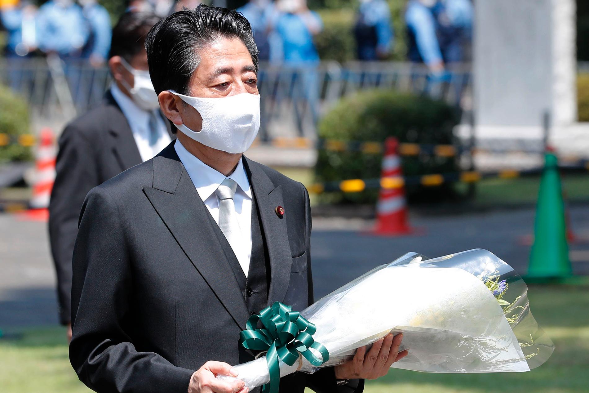 Premiärminister Shinzo Abe med munskydd och en blombukett under ett besök vid en kyrkogård med oidentifierade krigsoffer i Tokyo.