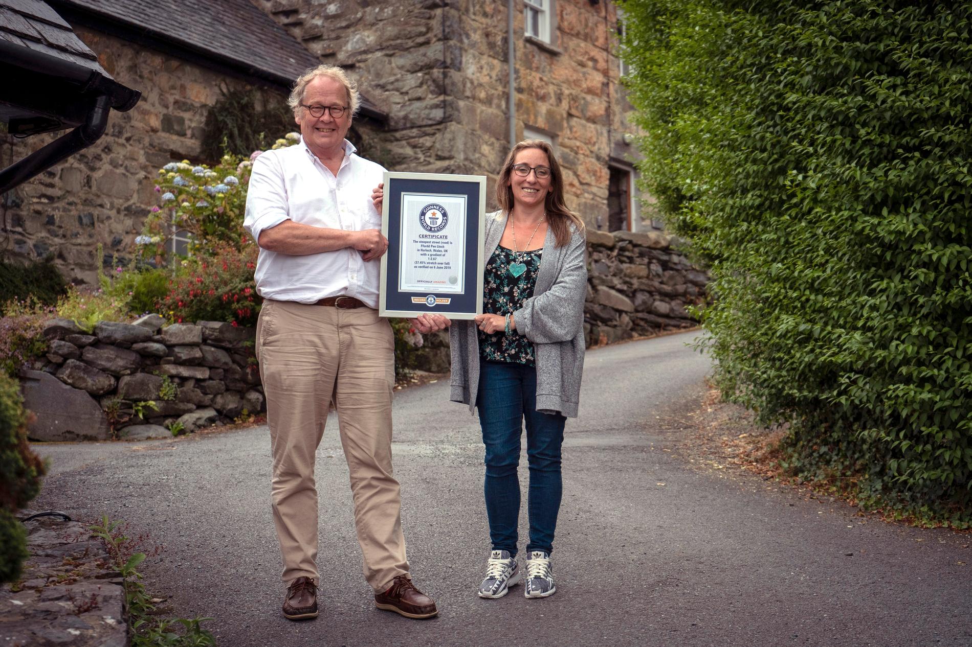 Gwyn Headley och Sarah Badhan står på Ffordd Pen Llech med ett diplom från Guinness rekordbok, som bekräftar att gatan är den brantaste i världen.