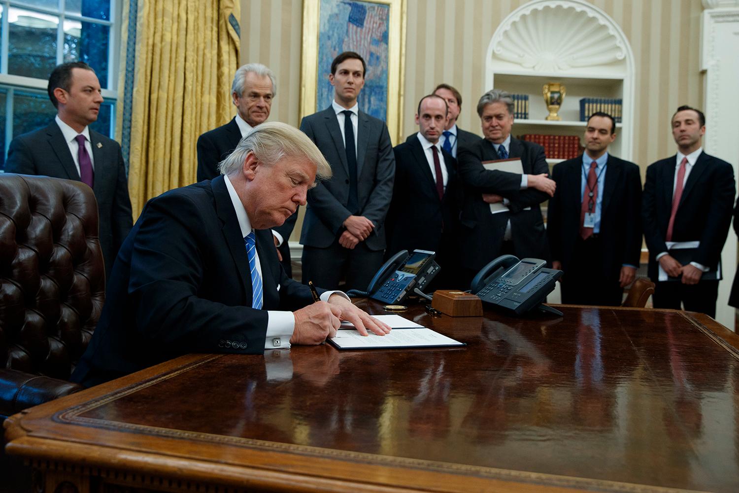 Här syns Banon som nummer tre från höger när Trump skriver en av sina presidentordrar.