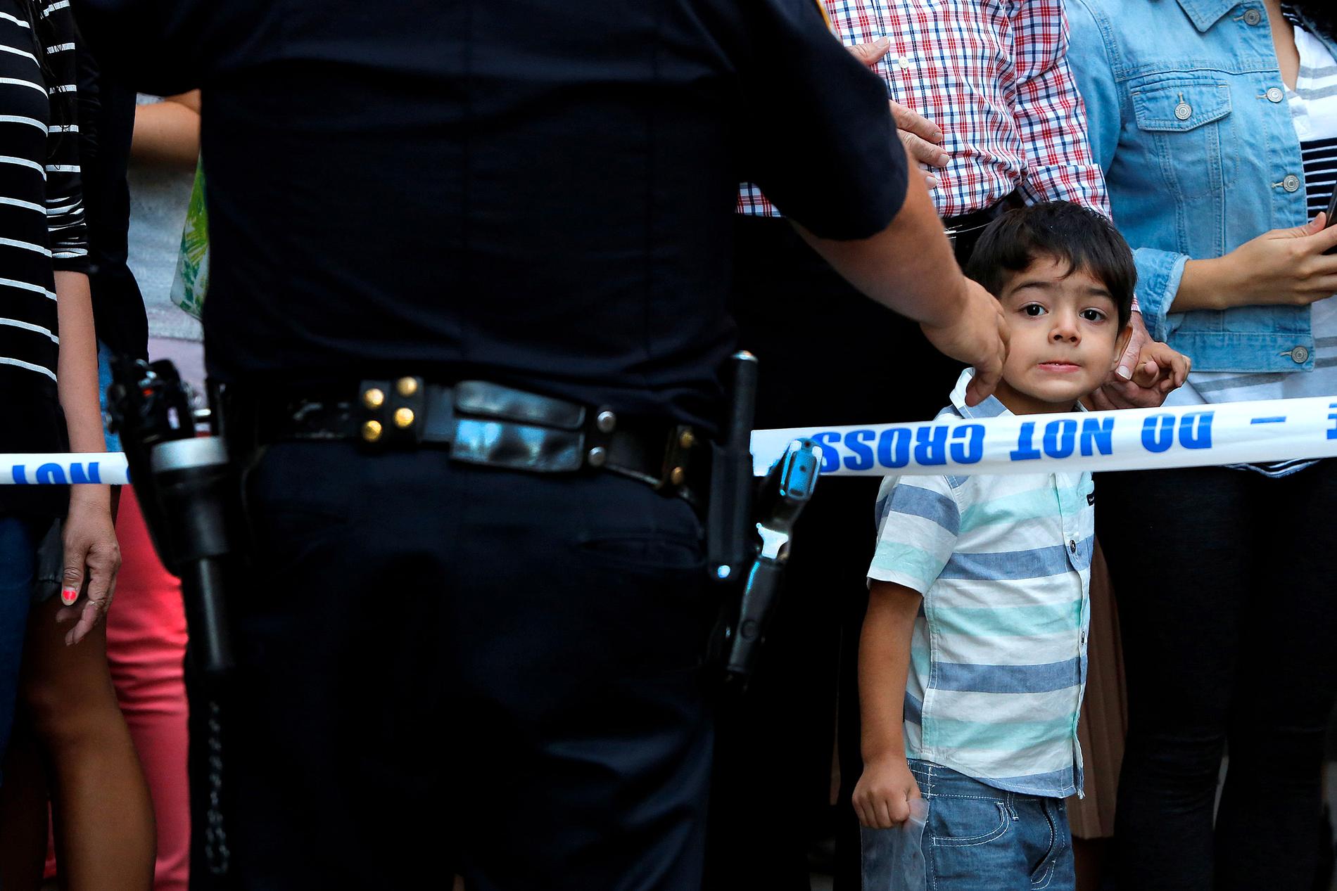 En pojke framme vid polisens avpärrningsband försöker få en glimt av vad som händer.