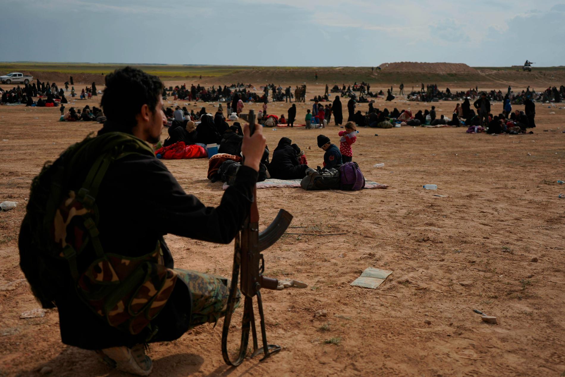En medlem i den kurdisk-arabiska milisen SDF vaktar människor som strömmat ut från IS-enklaven vid staden al-Baghuz i sydöstra Syrien.