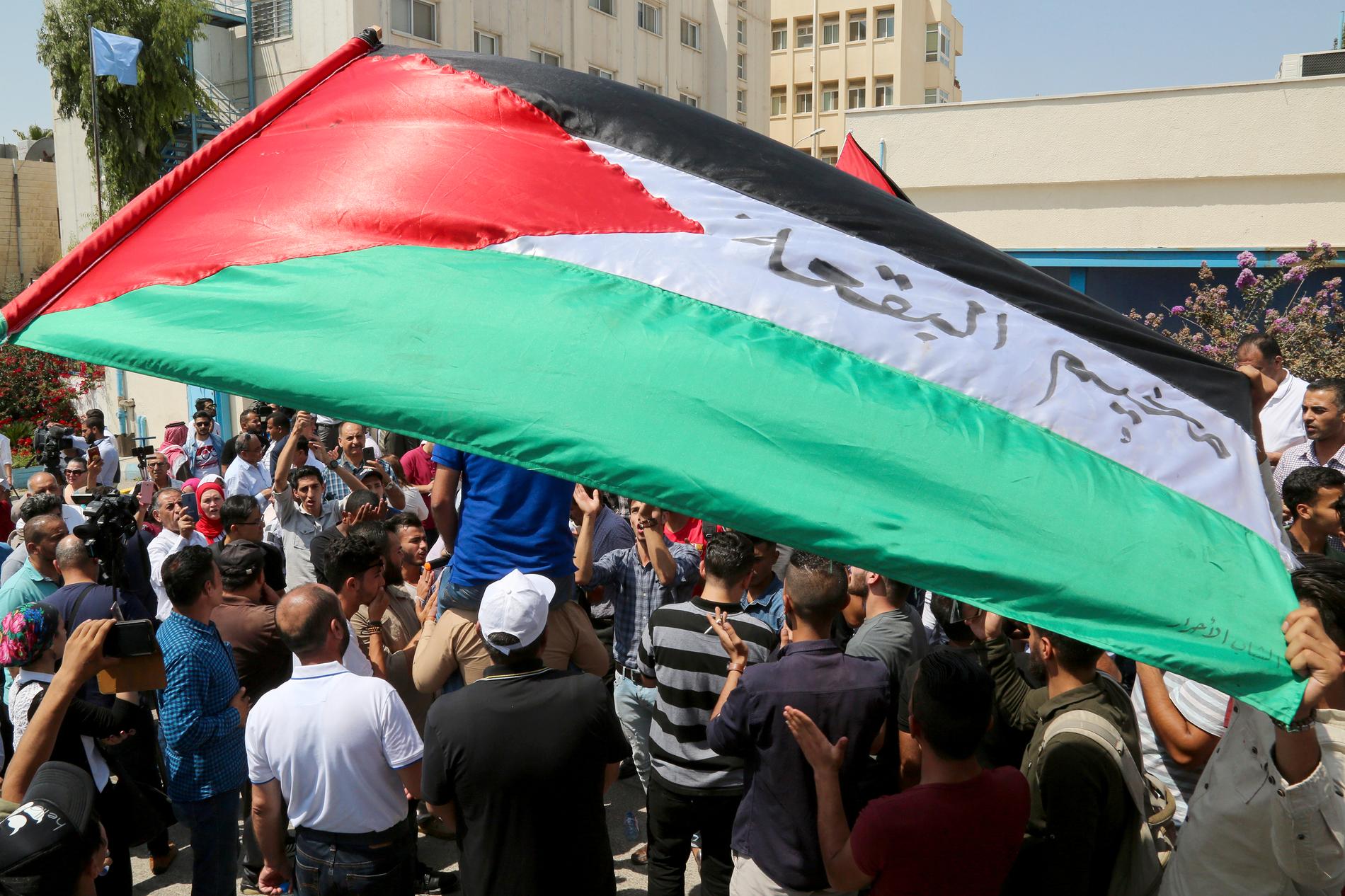Palestinska flyktingar håller upp flaggor och skanderar mot USA:s beslut att strypa bidrag till FN:s organ för palestinska flyktingar (UNRWA). Protesten ägde rum i Amman i Jordanien i söndags.