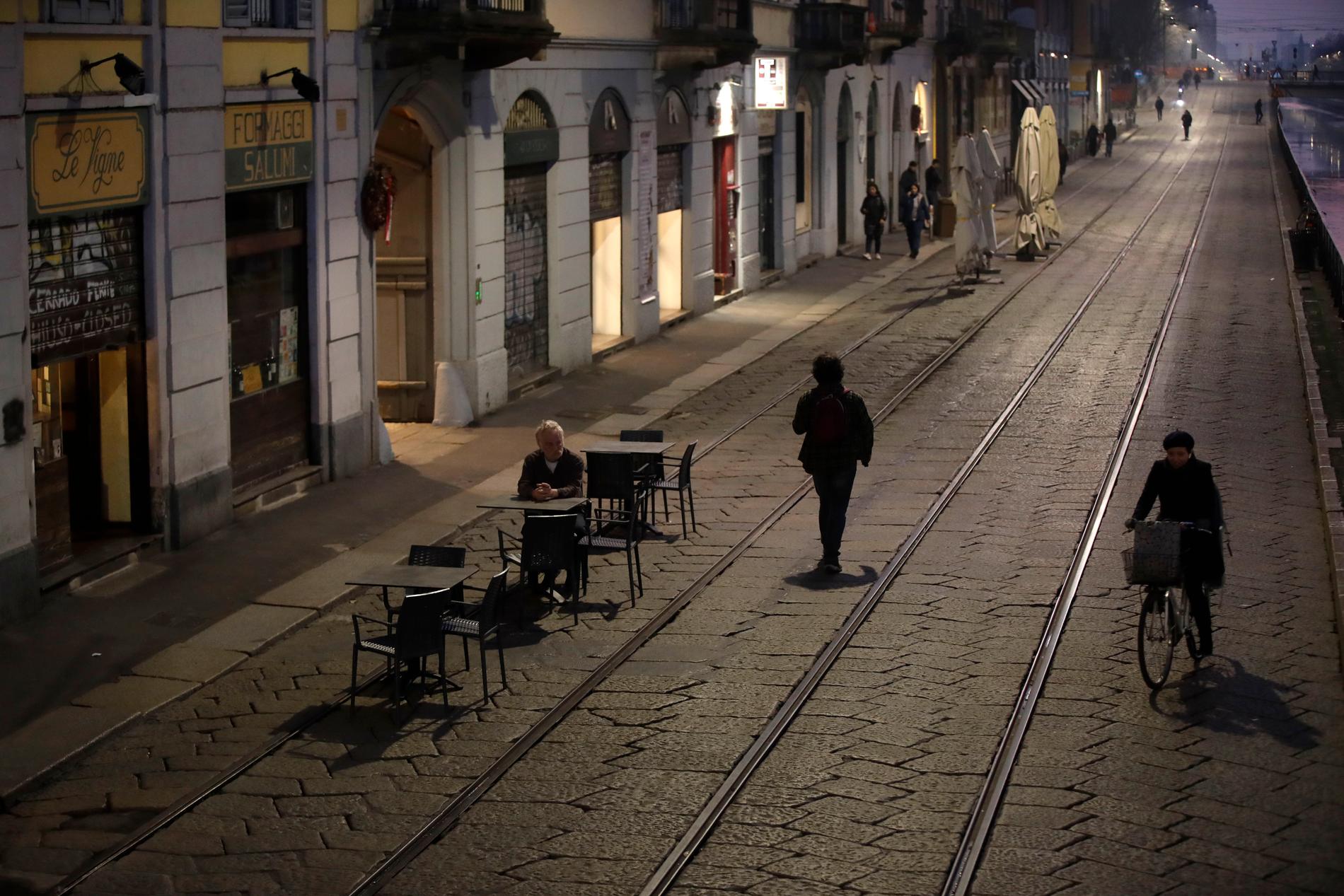 En man sitter ensam utanför en bar i Milano. Det rapporteras ha varit ovanligt stillsamt i storstaden med anledning av virusspridningen.