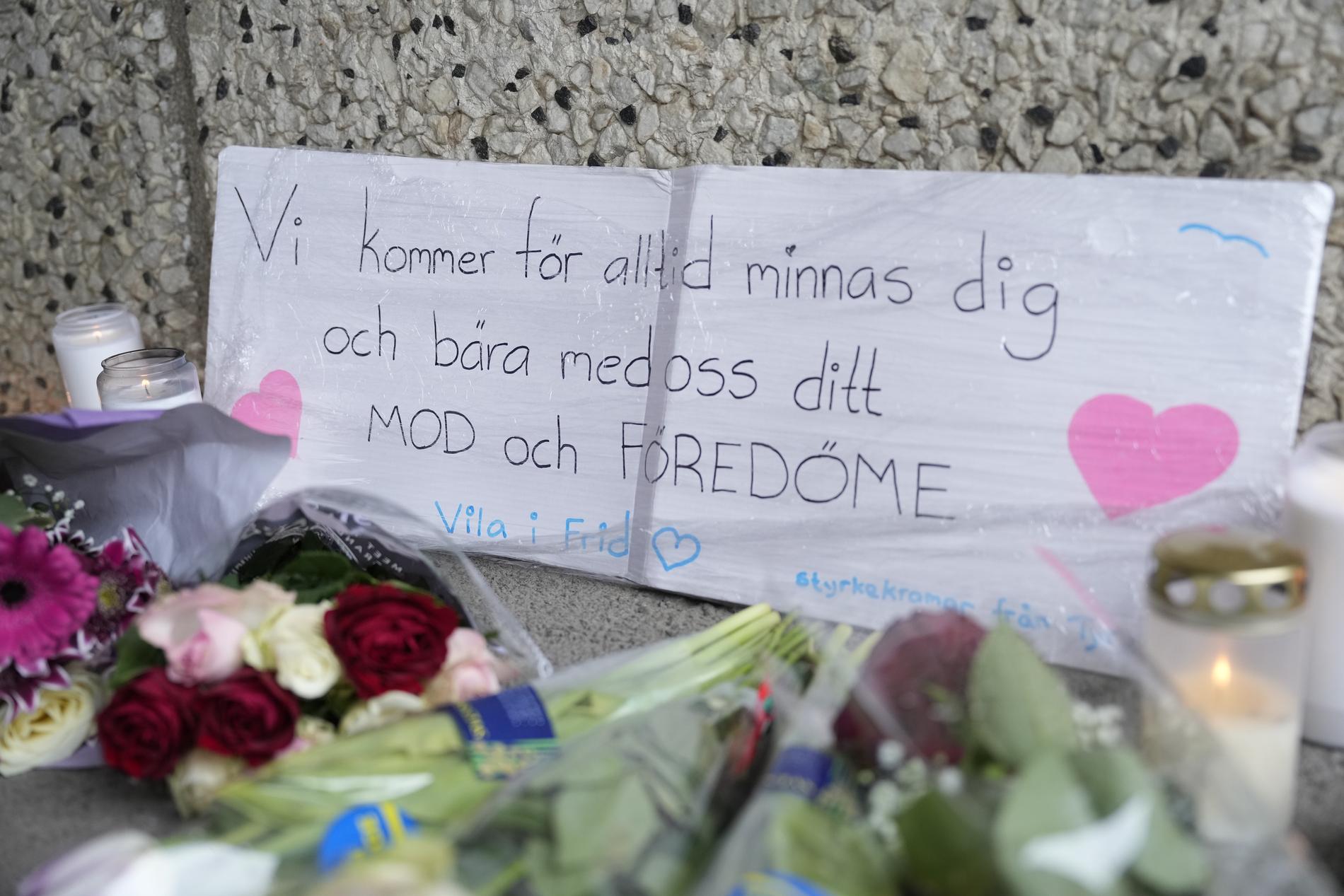 Blommor, gravljus och en skylt i gångtunneln i Skärholmen. På skylten står ”Vi kommer för alltid minnas dig och bära med oss ditt mod och föredöme. Vila i frid”