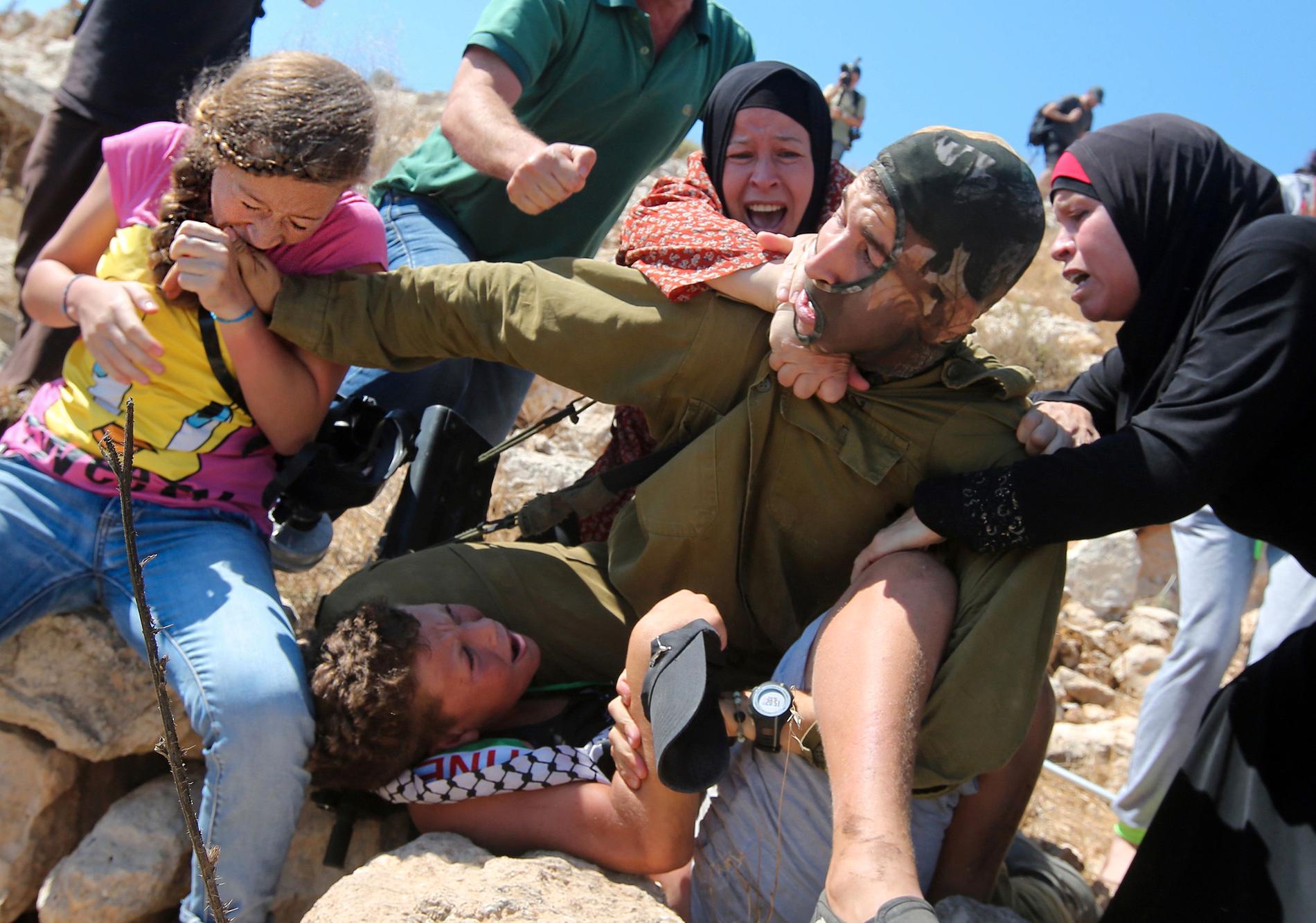 Ahed Tamimi biter en  israelisk soldat i armen.