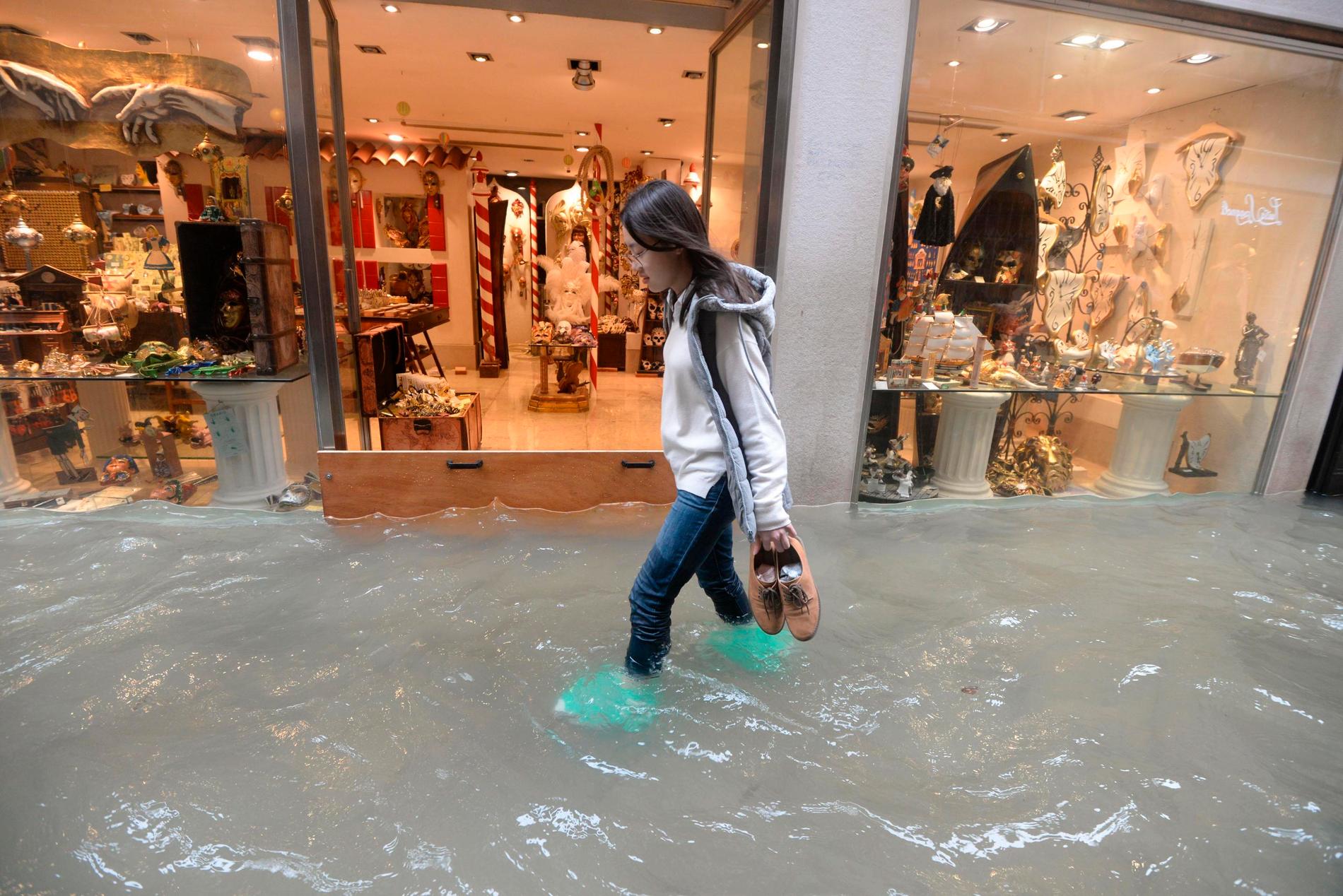 En kvinna vadar på en översvämmad gata i Venedig.