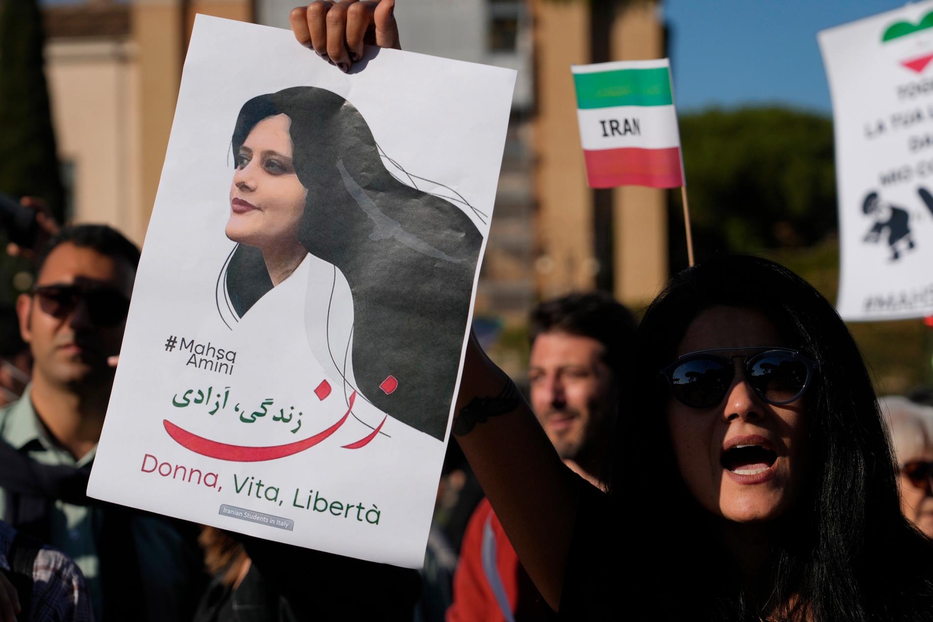 Demonstranter håller upp en skylt med en bild på Mahsa Zhina Amini, vars död i september utlöste de stora protester som skakat Iran sedan dess. Bilden är från en stöddemonstration i Rom. 