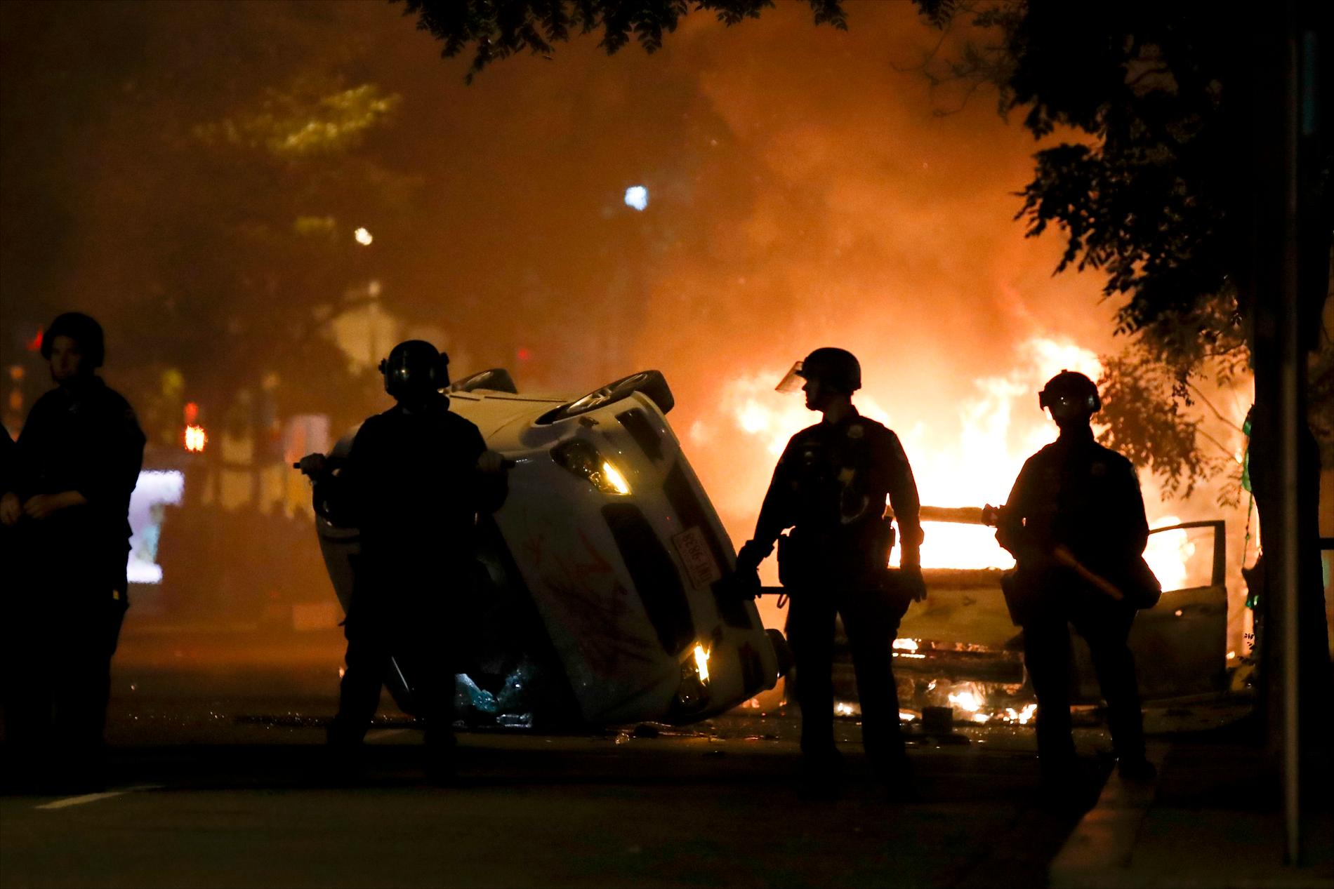 Poliser framför en sönderbränd bil nära Vita Huset där det var våldsamma protester under natten mot måndagen.