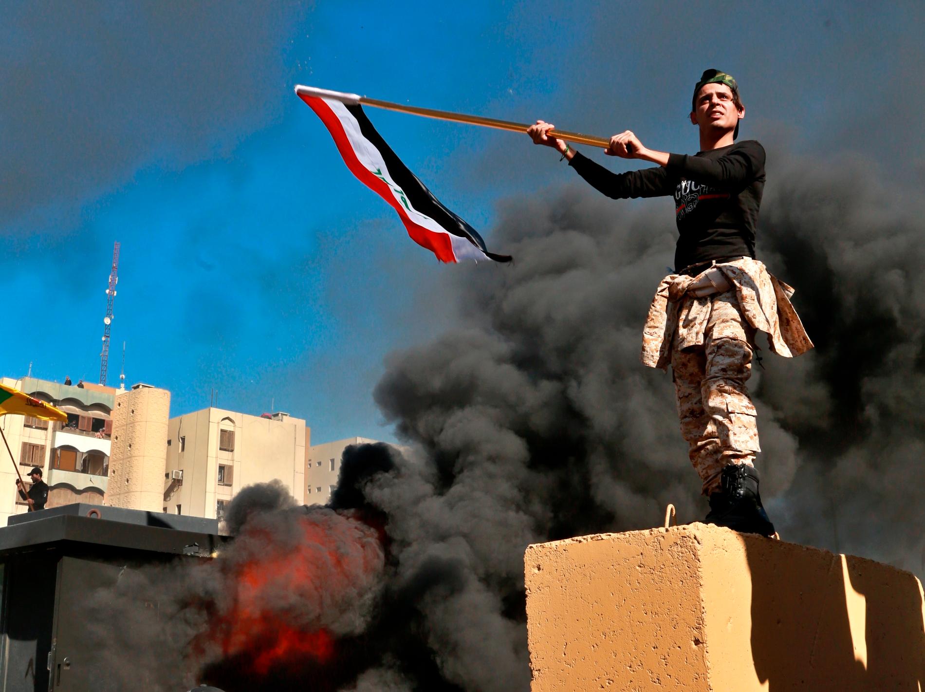 En demonstrant höjer den irakiska flaggan under protesterna utanför USA:s ambassad i Bagdad.