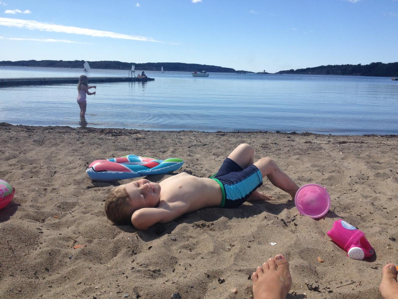 Ludvig, 3, ligger på stranden i Grebbestad och njuter av sommaren medan storasyster Isabelle, 6, badar.