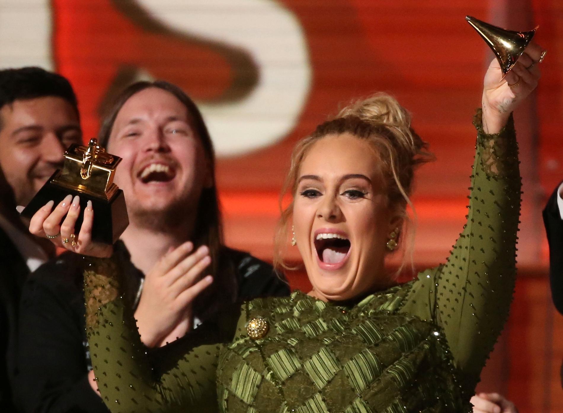 Adele glad med en av fem Grammystatyetter – den som gick sönder. I bakgrunden syns hennes svenska kollega, låtskrivaren Shellback.