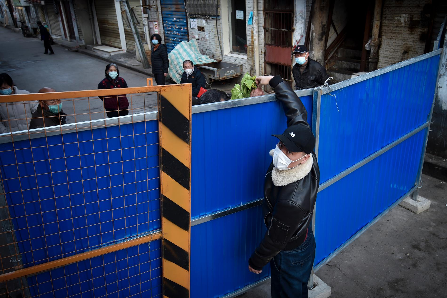 En man med ansiktsmask ger matvaror över staketet i ett område i Wuhan i februari. Arkivbild.