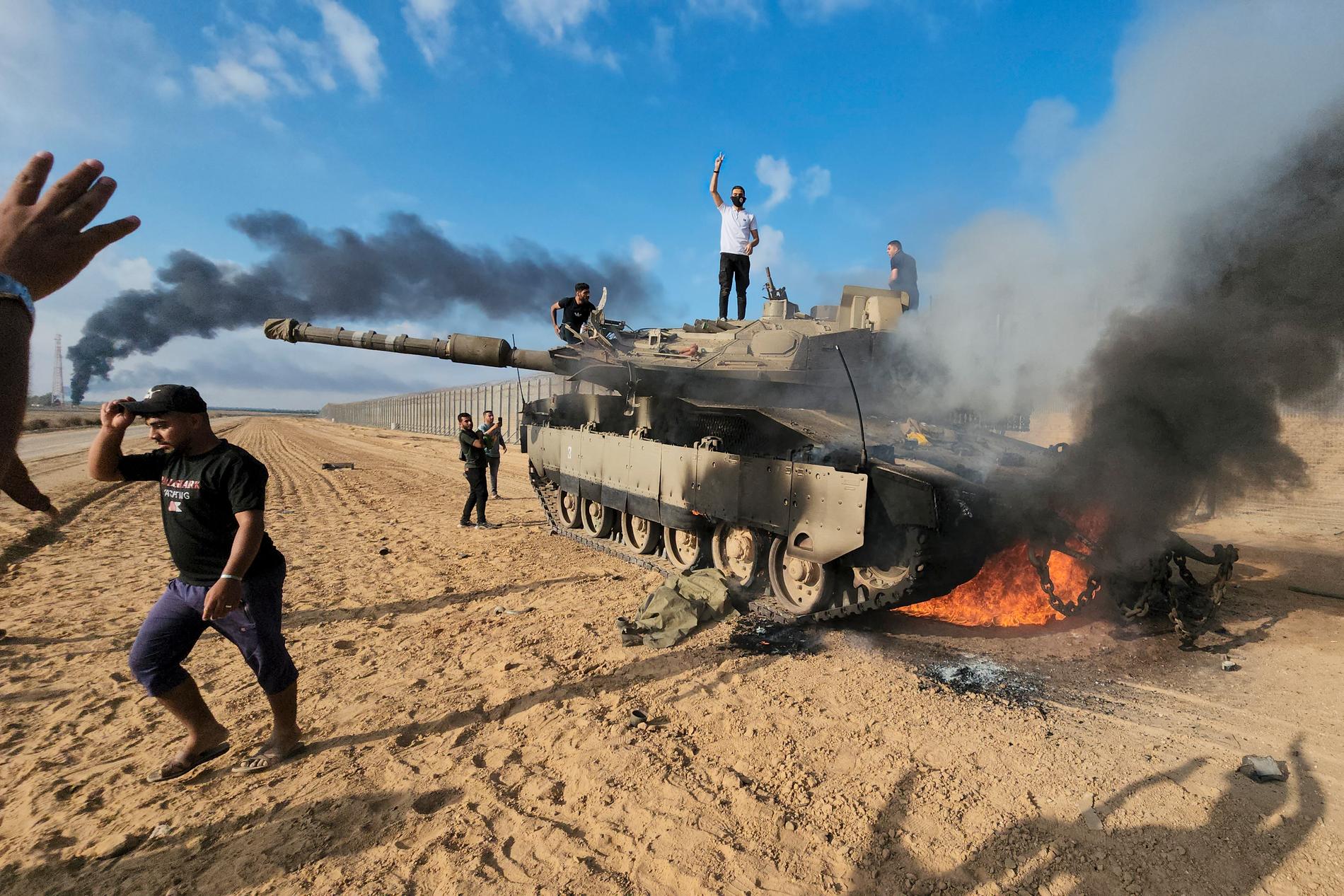 Människor står ovanpå en brinnande och förstörd israelisk stridsvagn vid Khan Yunis i Gazaremsan.