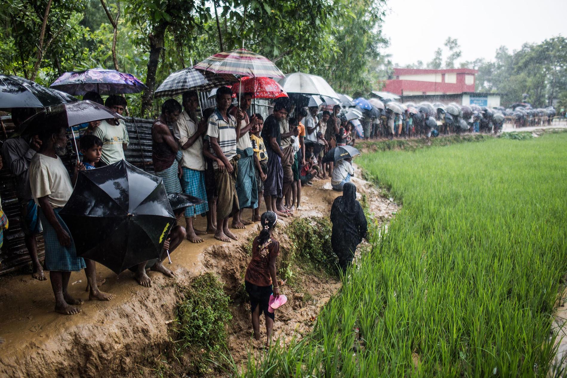 Flyktingar väntar i hällregnet på bistånd.