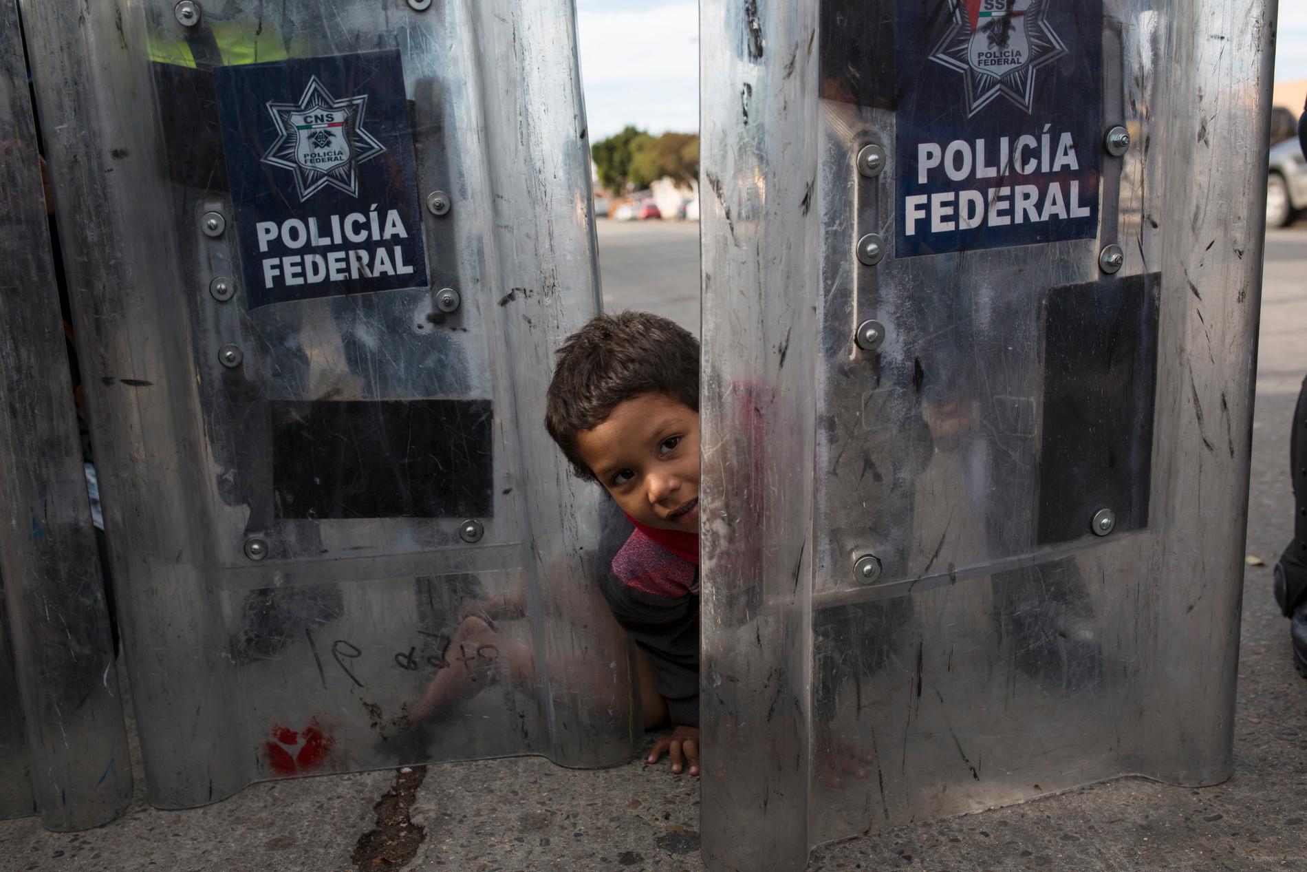 Treåriga Elias Lopez från Honduras leker mellan den mexikanska kravallpolisens sköldar i närheten av gränsövergången El Chaparral i Tijuana, där hundratals migranter under torsdagen genomförde en fredlig manifestation med krav på att bli insläppta i USA.