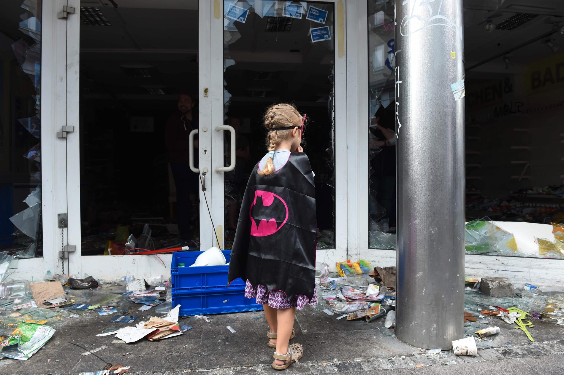 En flicka i batmandräkt står utanför ett plundrat apotek i Schanzenviertel-distriktet i Hamburg.