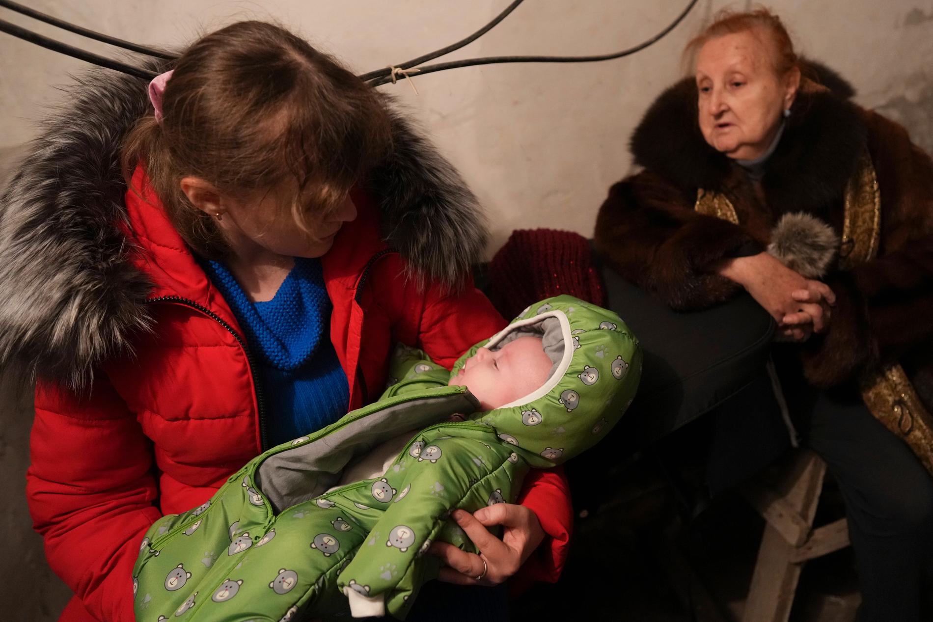 En kvinna vaggar sin sovande bebis i ett skyddsrum i Mariopol under ryskt bombardemang. 