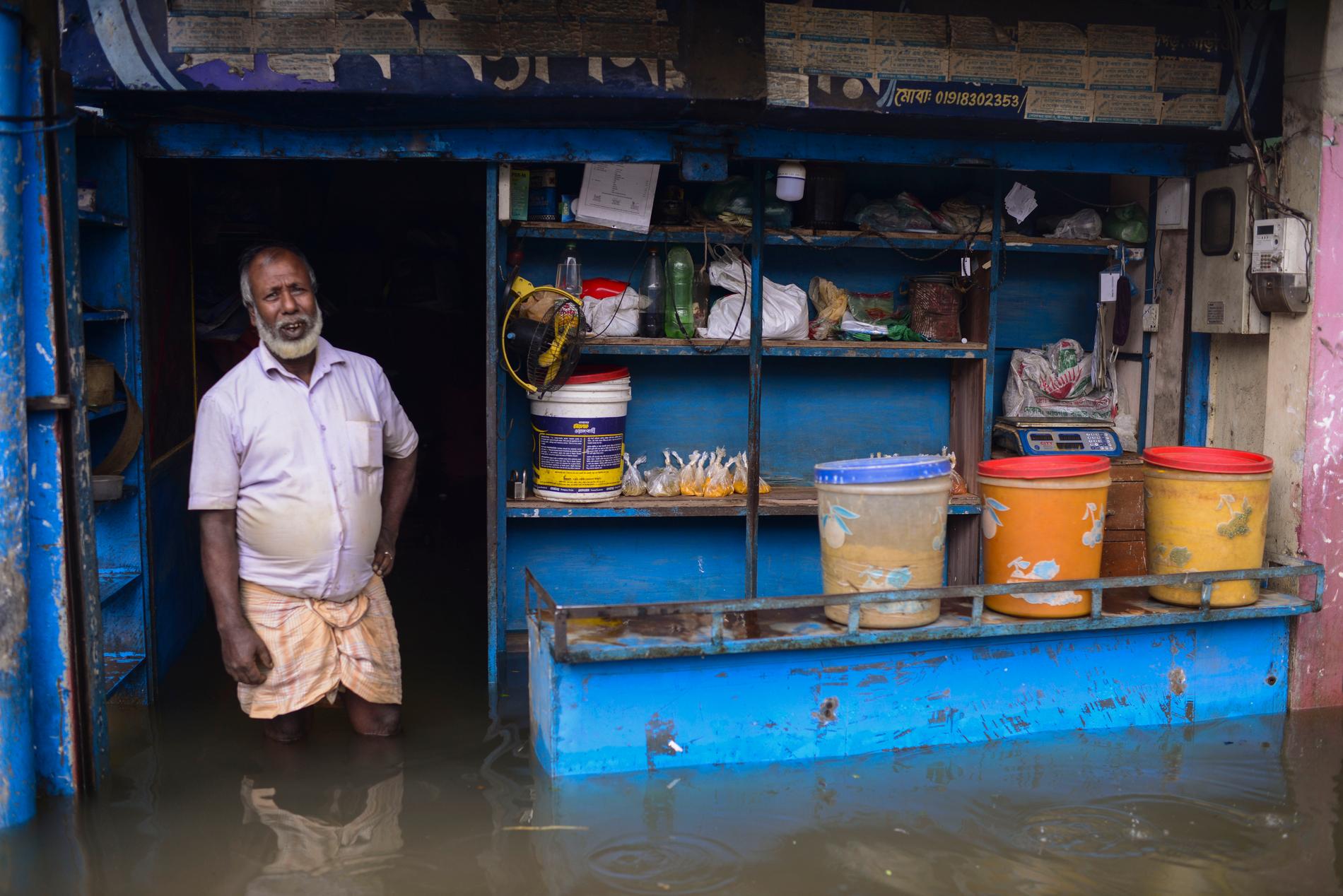 En man står i dörröppningen till sin översvämmade affär i Sylhet, Bangladesh.