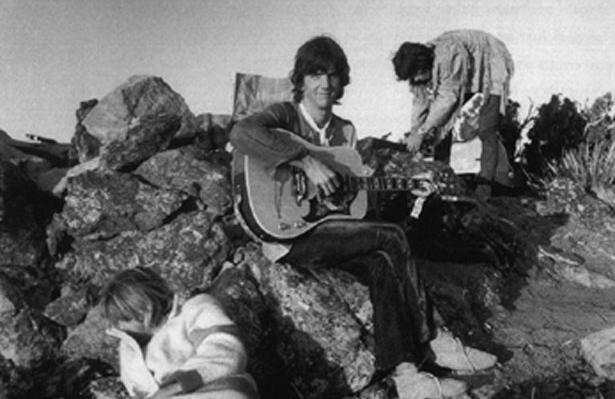 Gram Parsons spelar gitarr på klippa vid Joshua Tree. I bakgrunden Keith Richards.