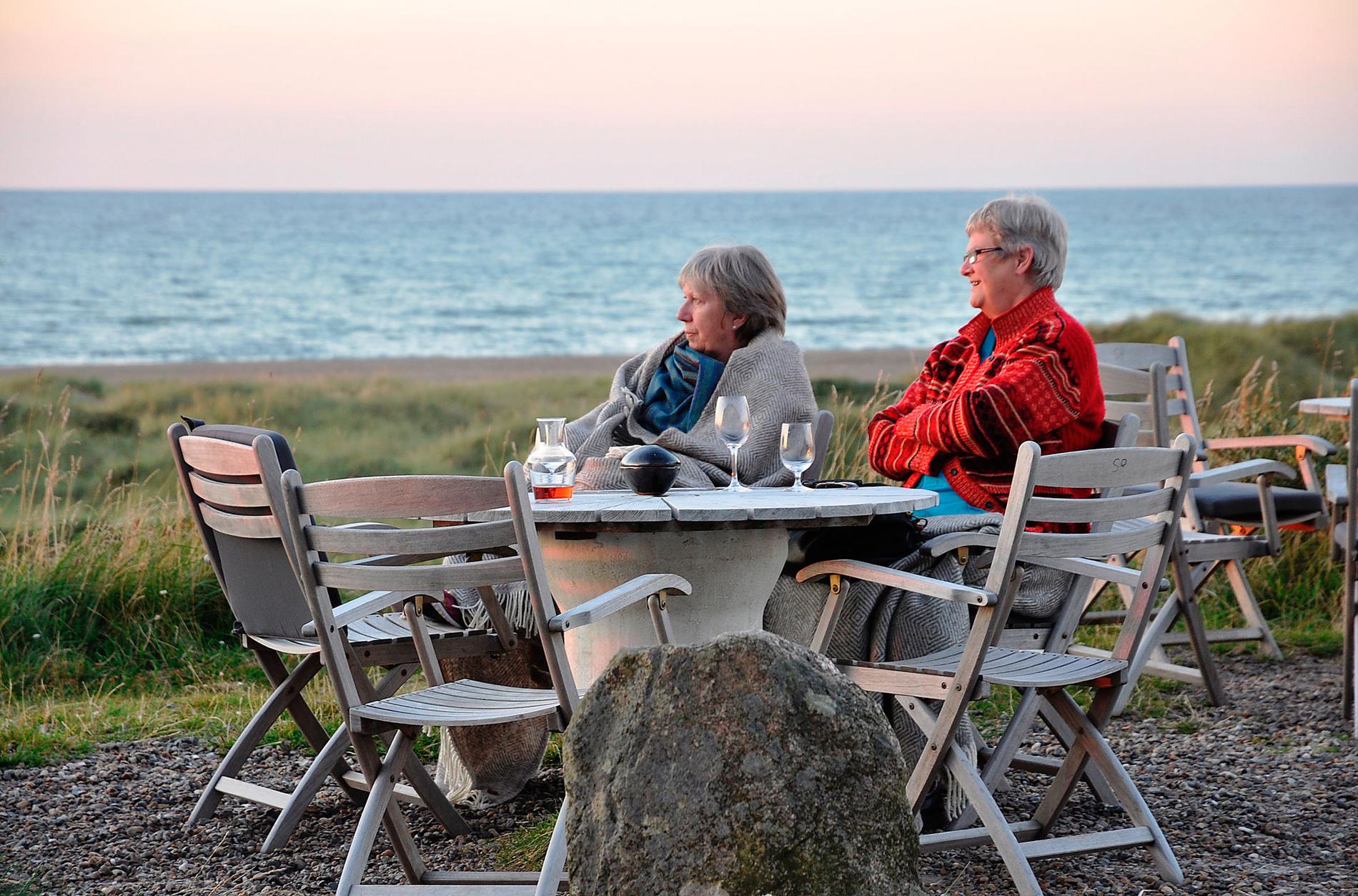 Väninnorna Tove och Sonja beundrar solnedgången vid Svinkløv över ett glas vin.