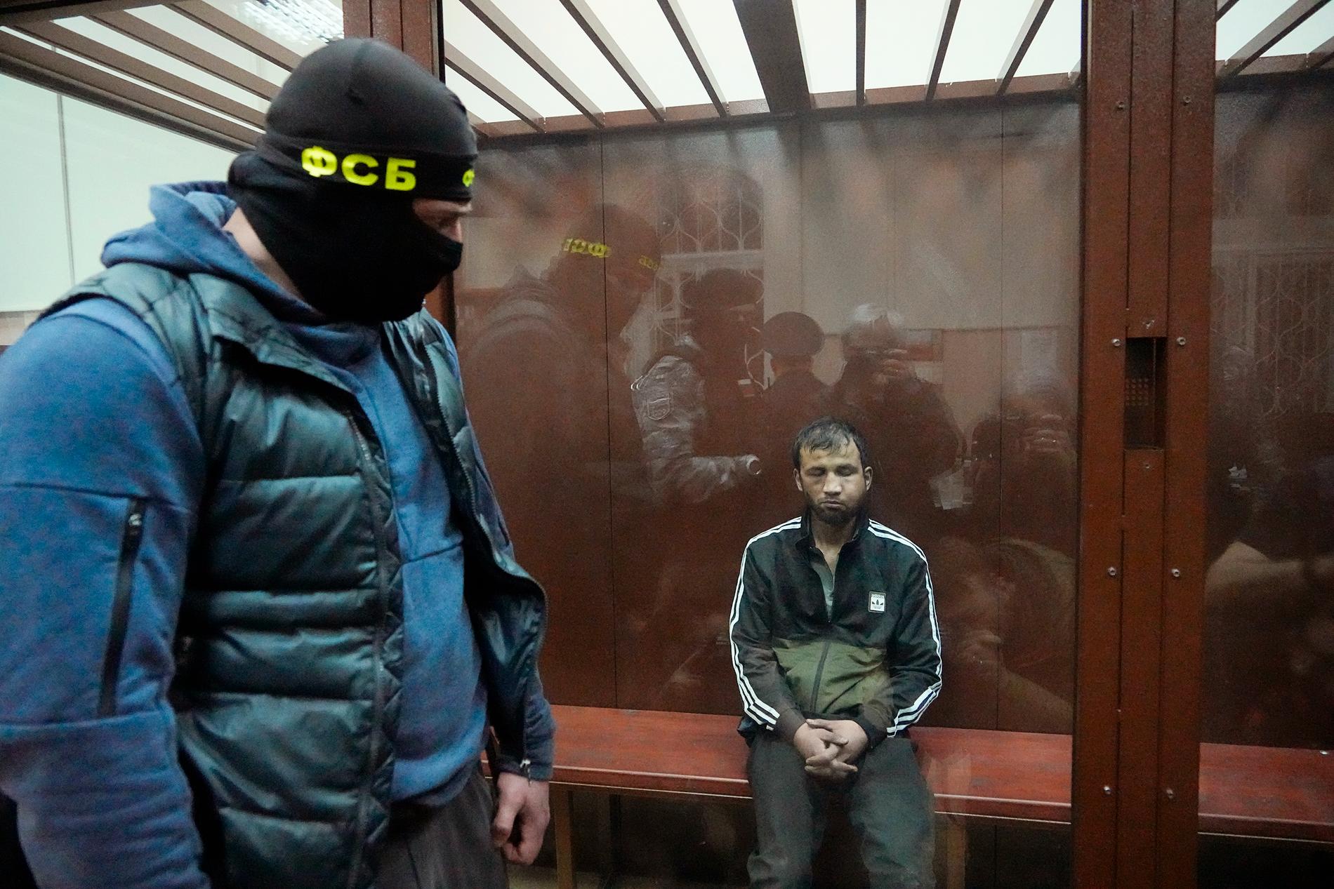 Sjamsidin Fariduni, en av de fyra män som misstänks ha varit med och dödat fler än 130 människor i Moskva i fredags. I förgrunden står en maskerad man från säkerhetstjänsten FSB.