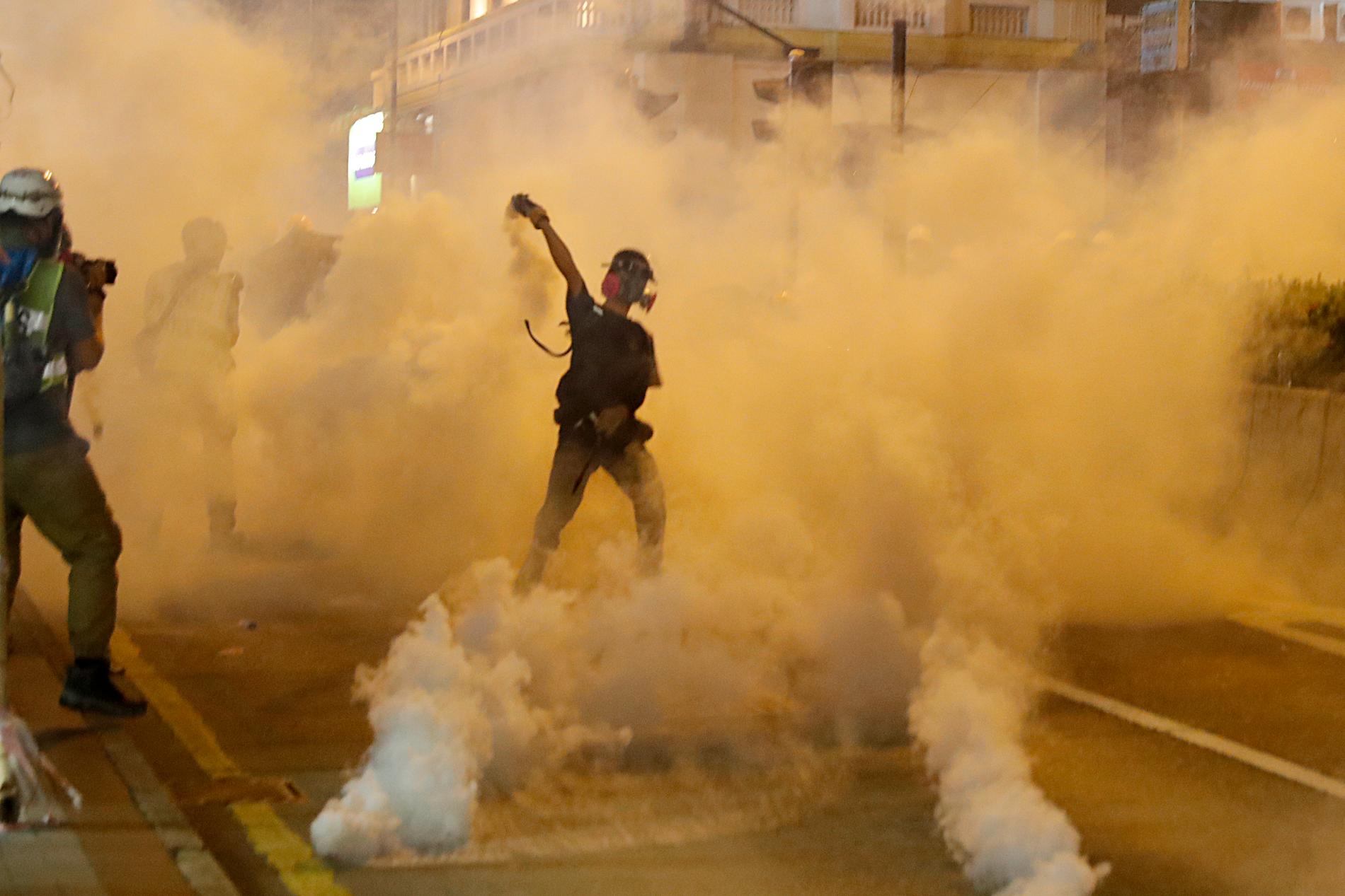En demonstrant kastar tillbaka en av polisens tårgasgranater under lördagens sammandrabbningar.