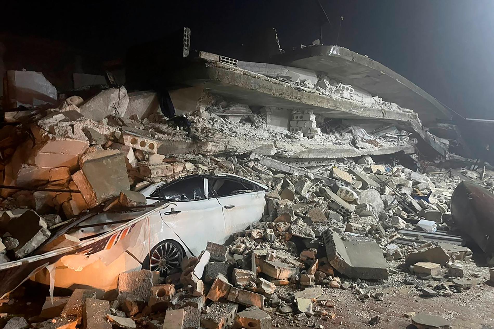 En bil har krossats under rasmassorna av en byggnad i Azmarin, i norra Syrien. 