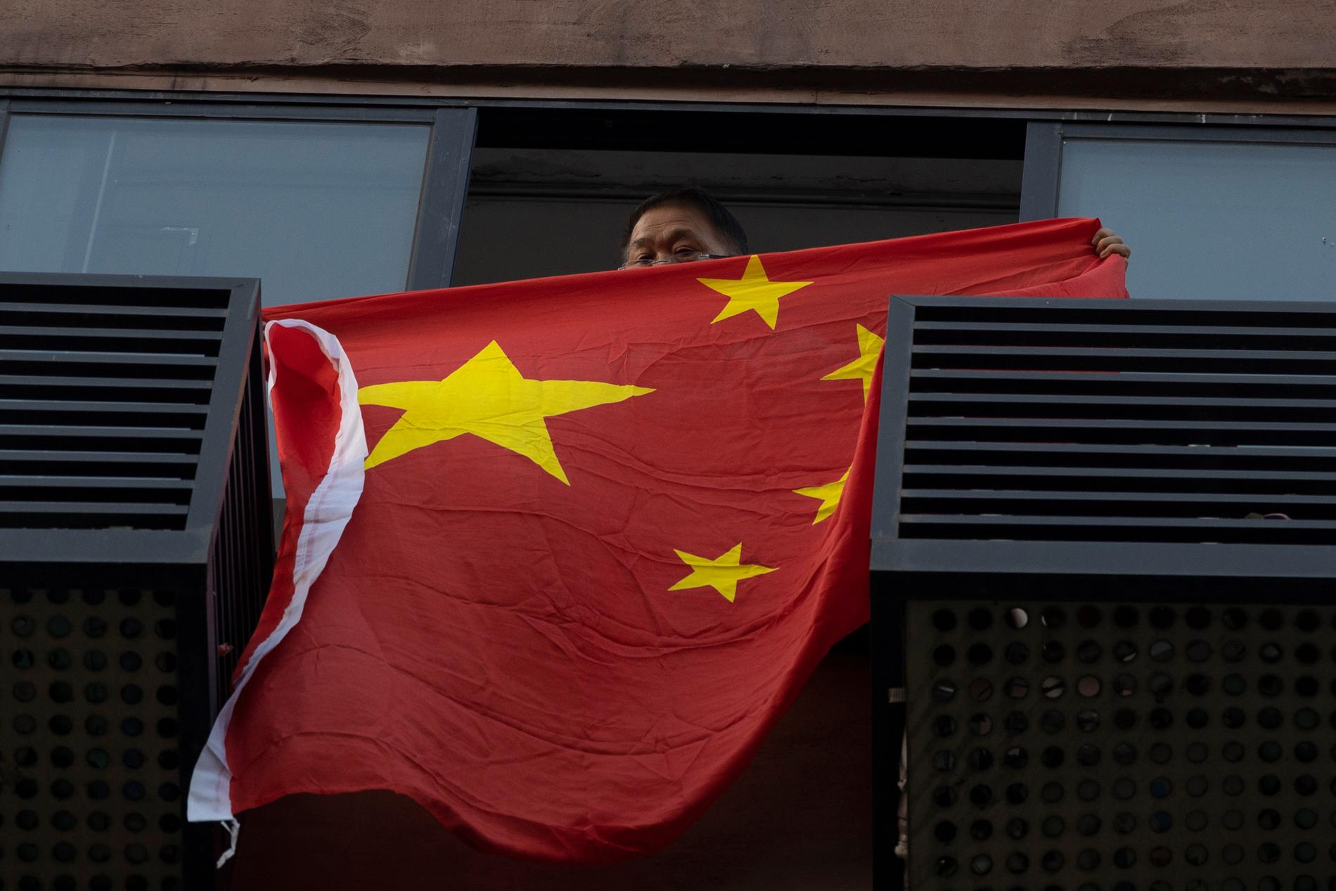 En boende rullar ut en kinesisk flagga från en lägenhet mitt emot konsulatet.