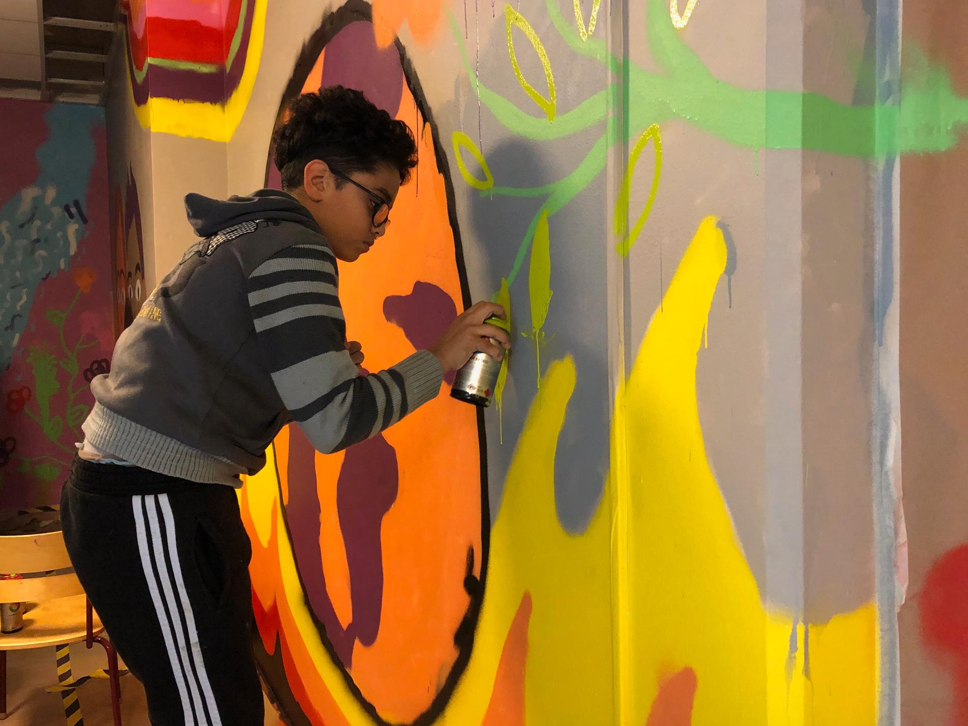 Mohammed Refai sprayar noggrant på gul färg på muralmålningen.