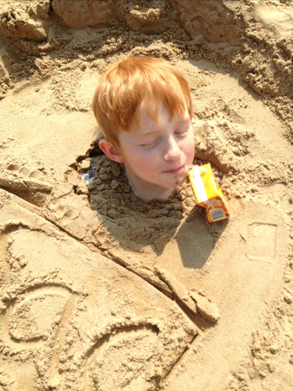 Sommarbild med Isac nergrävd i sanden av en kompis.