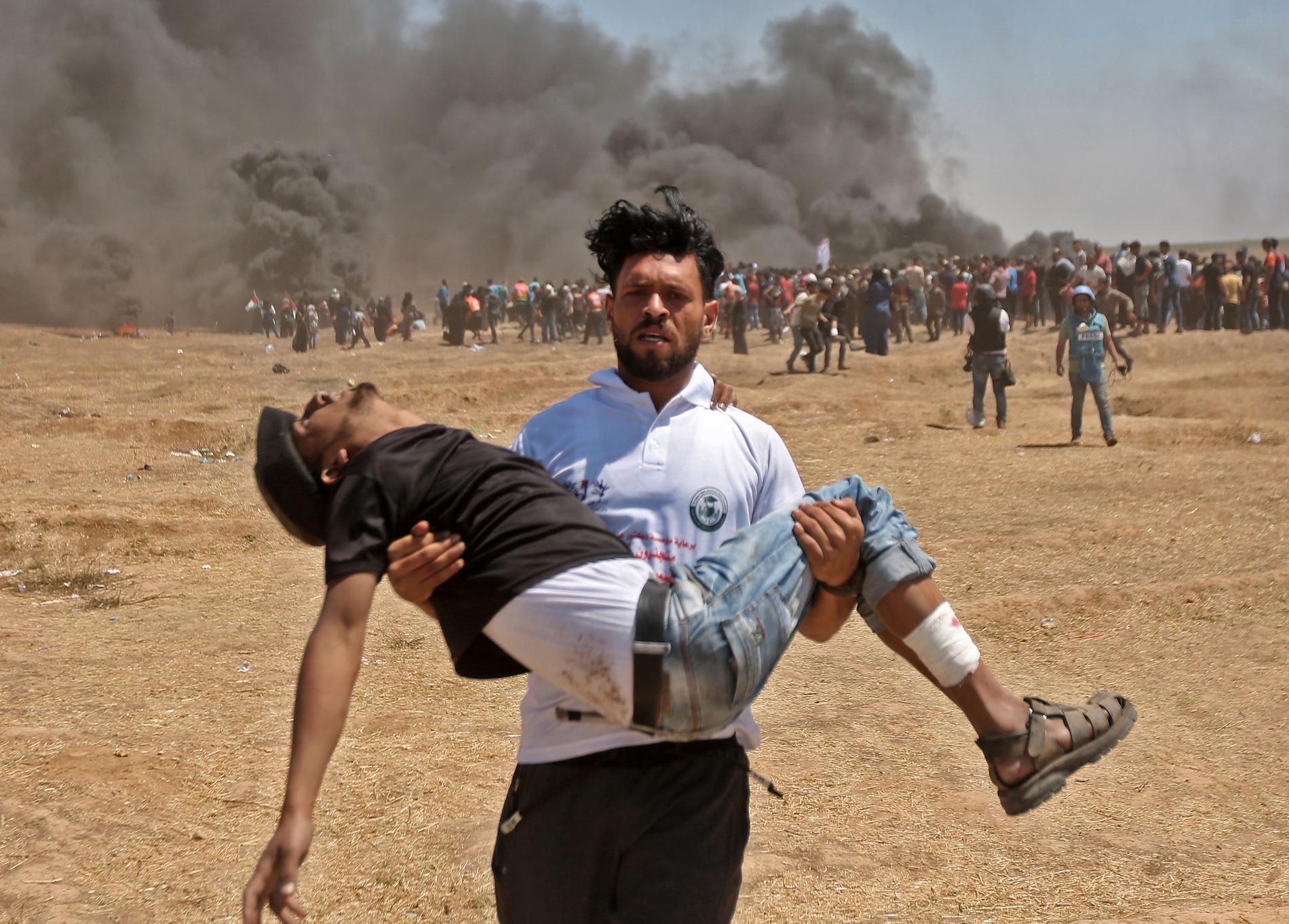 En palestinsk man bär en sårad demonstrant efter sammandrabbningar med israelisk militär vid Gazaremsan. 