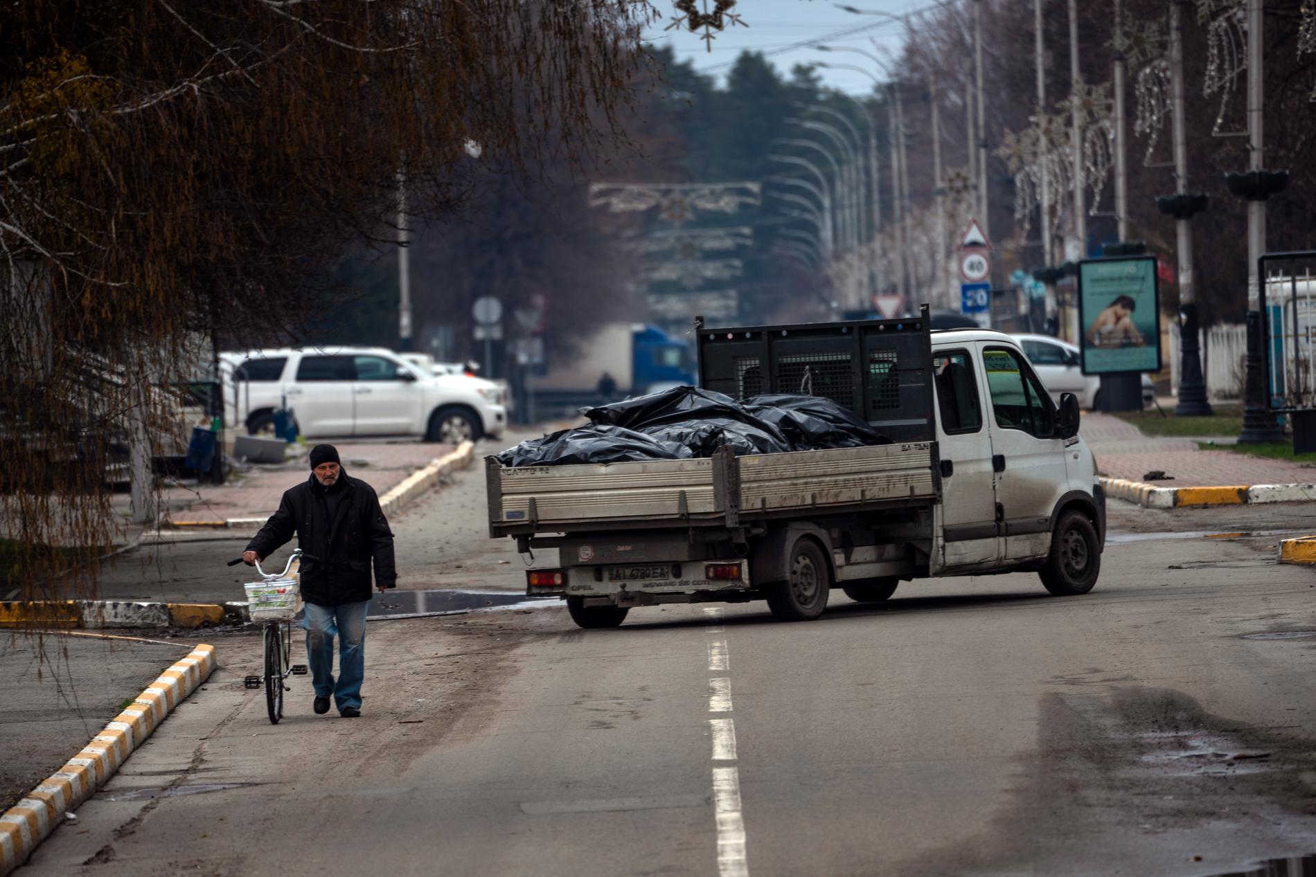 En man med cykel går förbi en lastbil som transporterar döda i Butja. 