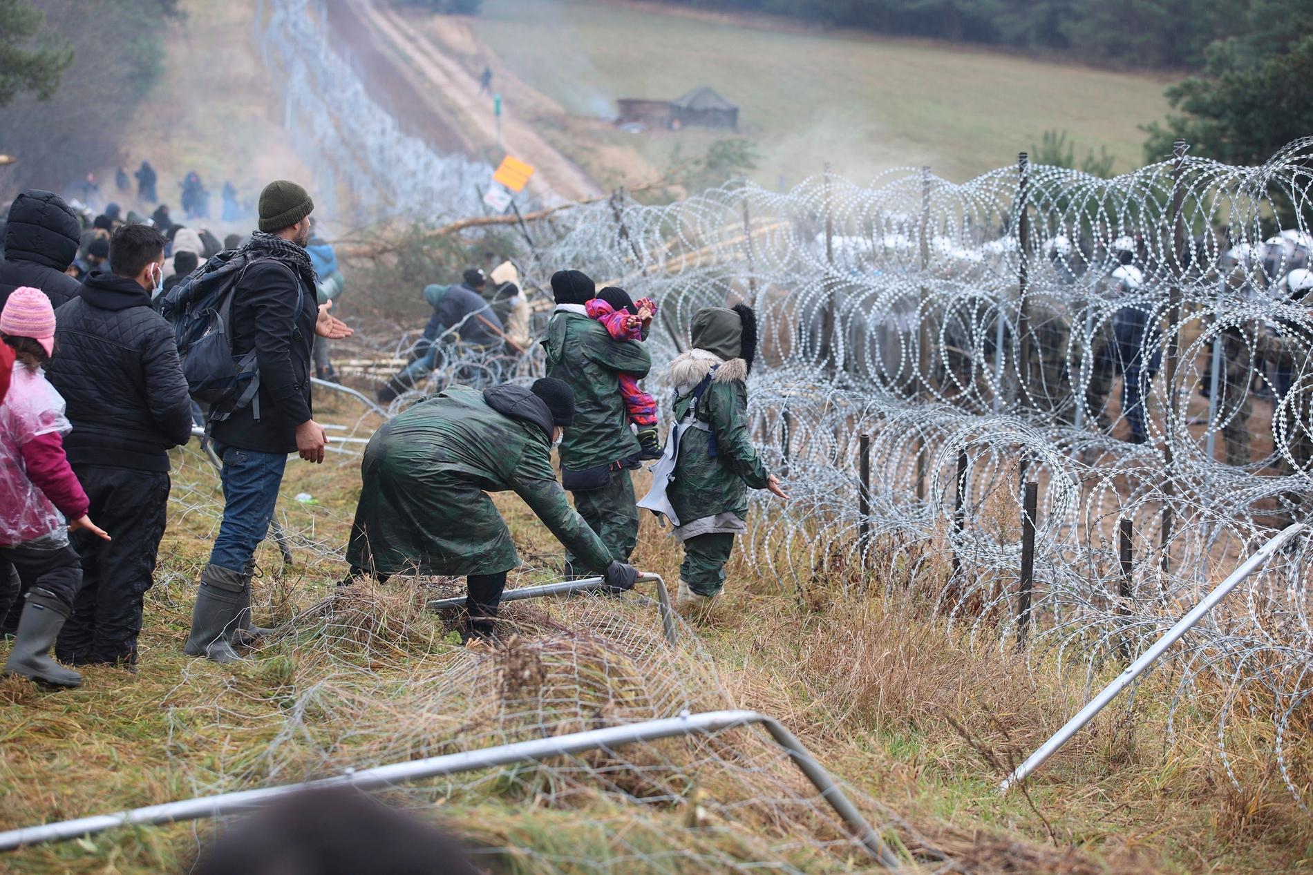 Migranter med barn vid gränsen Belarus–Polen. På andra sidan syns de polska soldaternas vita hjälmar.