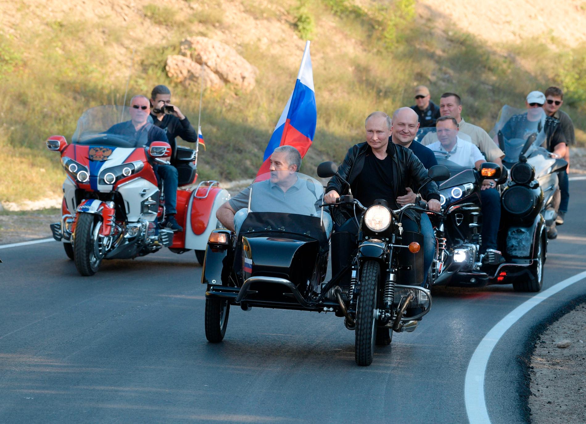 Vladimir Putin bakom styret på en Ural-motorcykel med sidovagn. I sidovagnen sitter Sergej Aksionov, premiärminister på Krim. På bönpallen fick Mikhail Razvozhaev, guvernör i Sevastopol, sitta.
