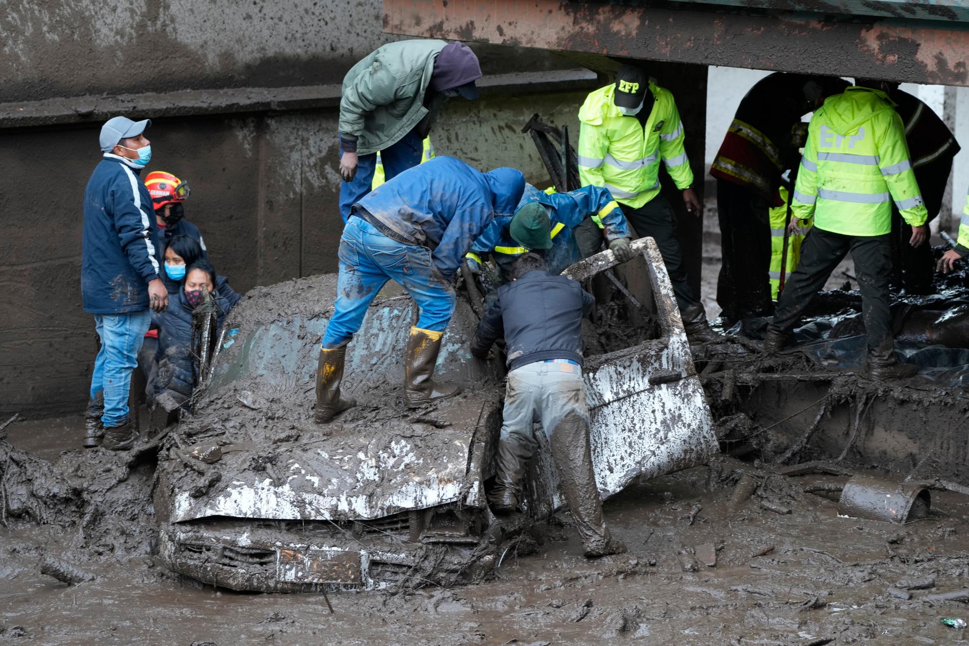 Räddningsarbetare kontrollerar att det inte finns människor i en bil som svepts med av lera efter jordskredet. 
