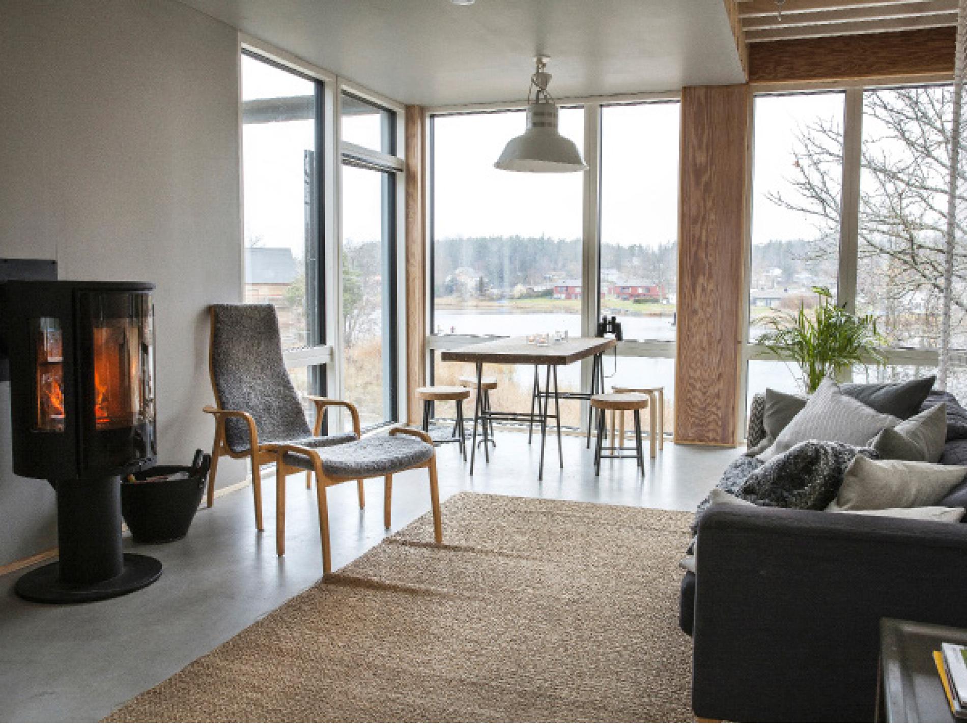 Vardagsrummet med fönster från golv till tak och utgång till terrass i västerläge. Kaminen  från Contura är husets hjärta, bredvid den en laminofåtölj. Matbord och pallar i kork från Ikea.
