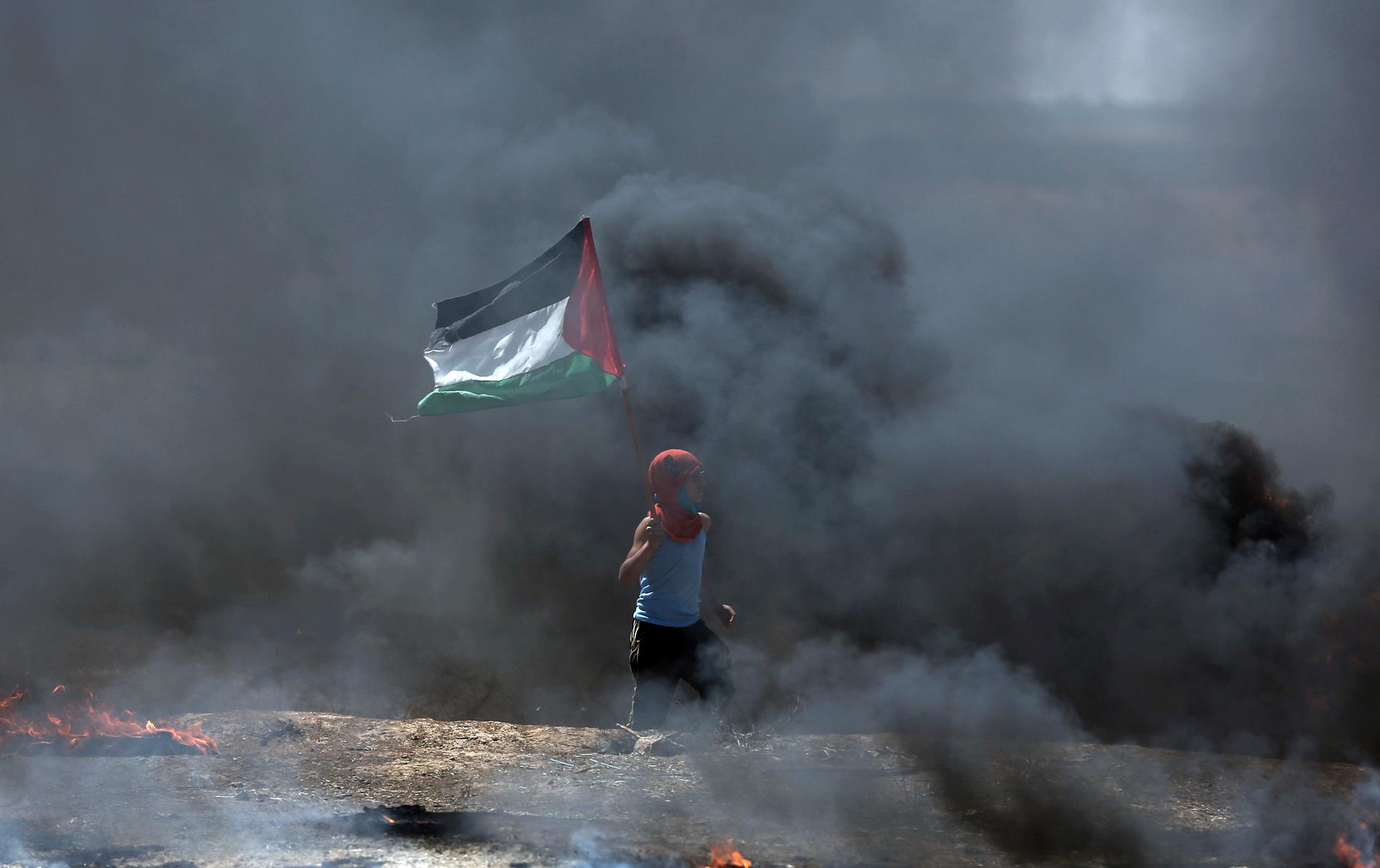 En pojke viftar med en palestinska flagga medan han passerar genom den svarta röken från brinnande bildäck vid Gazas gräns mot Israel.