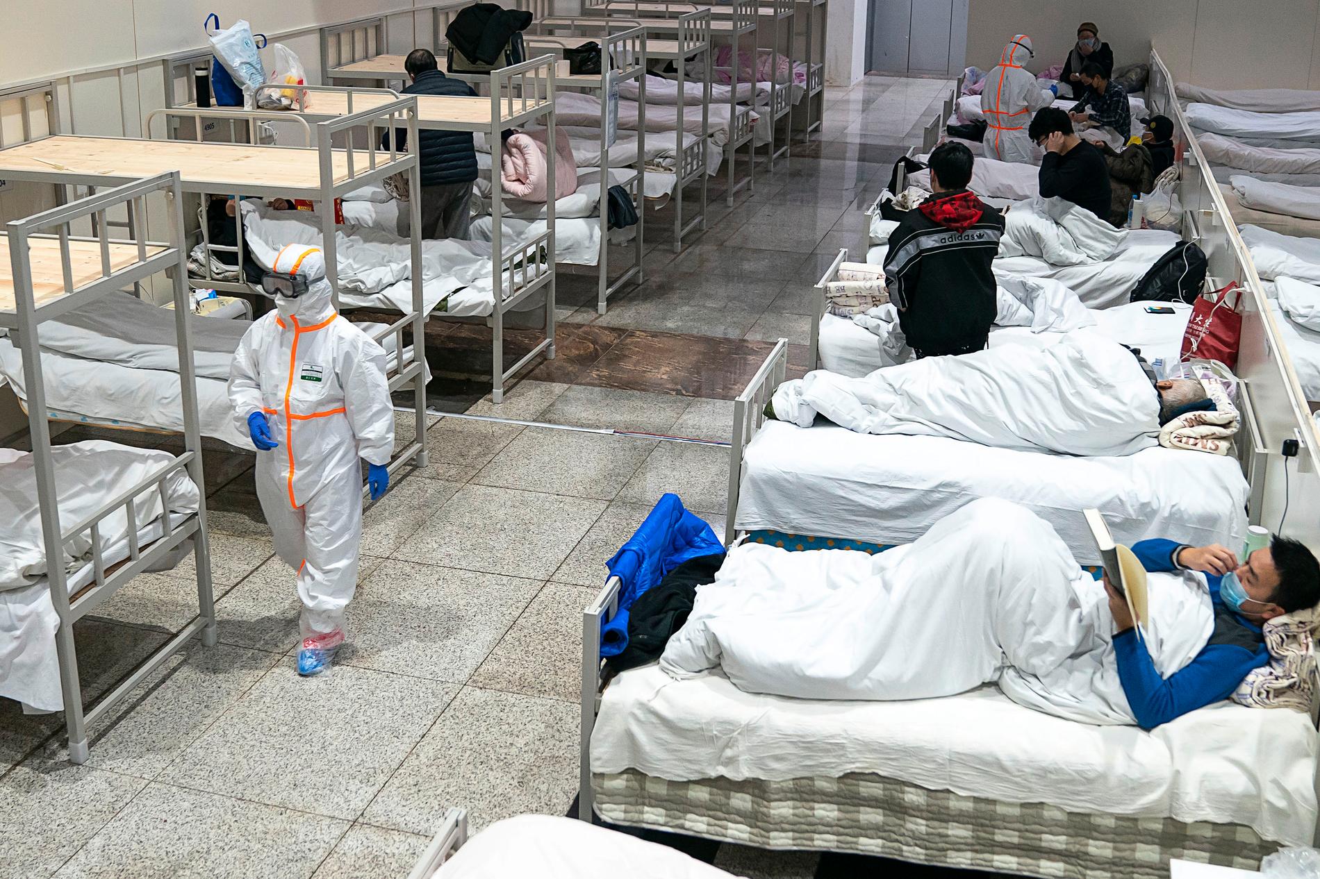 En sjukvårdsarbetare i skyddsdräkt går förbi patienter smittade med det nya coronaviruset i en utställningslokal som gjorts om till sjukhus i Wuhan i Kinas värst drabbade provins Hubei på onsdagen.