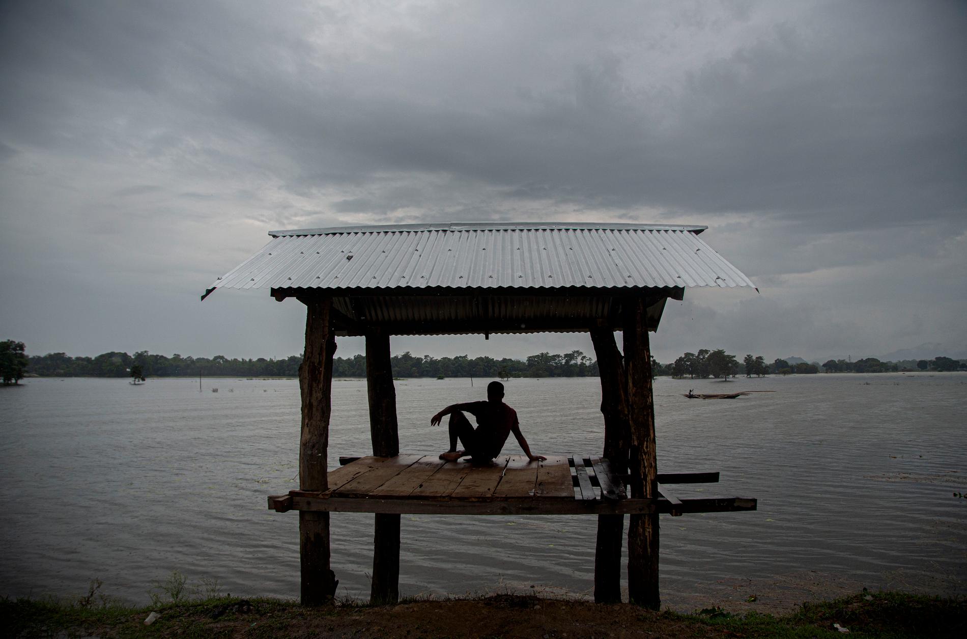 En man sitter intill översvämningen i Morigaon i Assam i Indien. Kraftiga skyfall har gjort att floden Brahmaputra som flyter genom Indien och Bangladesh svämmat över och lett till några av de värsta översvämningarna på årtionden.