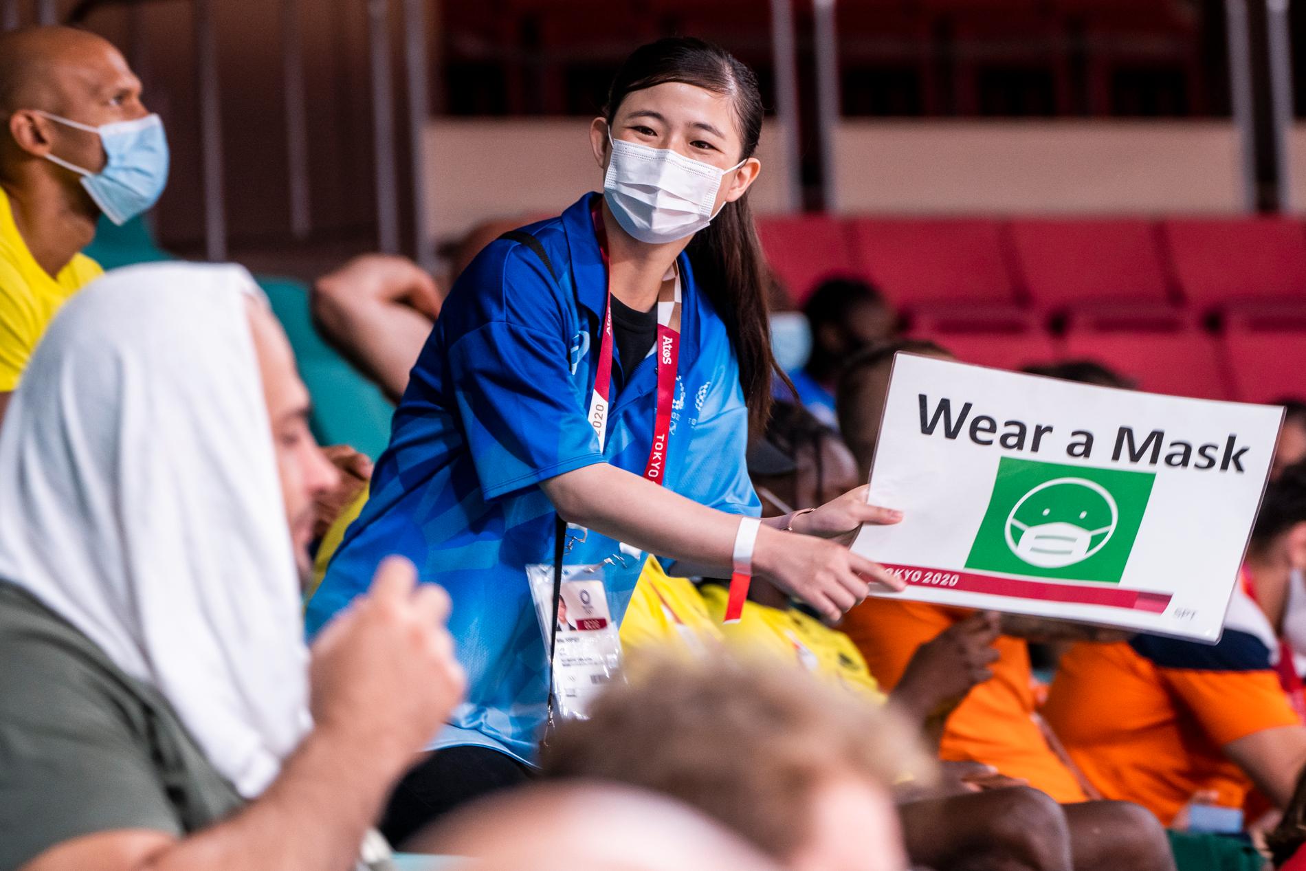 En funktionär håller upp en skylt om att de måste bära munskydd. Tränare och andra aktiva skriker i arenan Nippon Budakan under Sommar-OS i Tokyo.